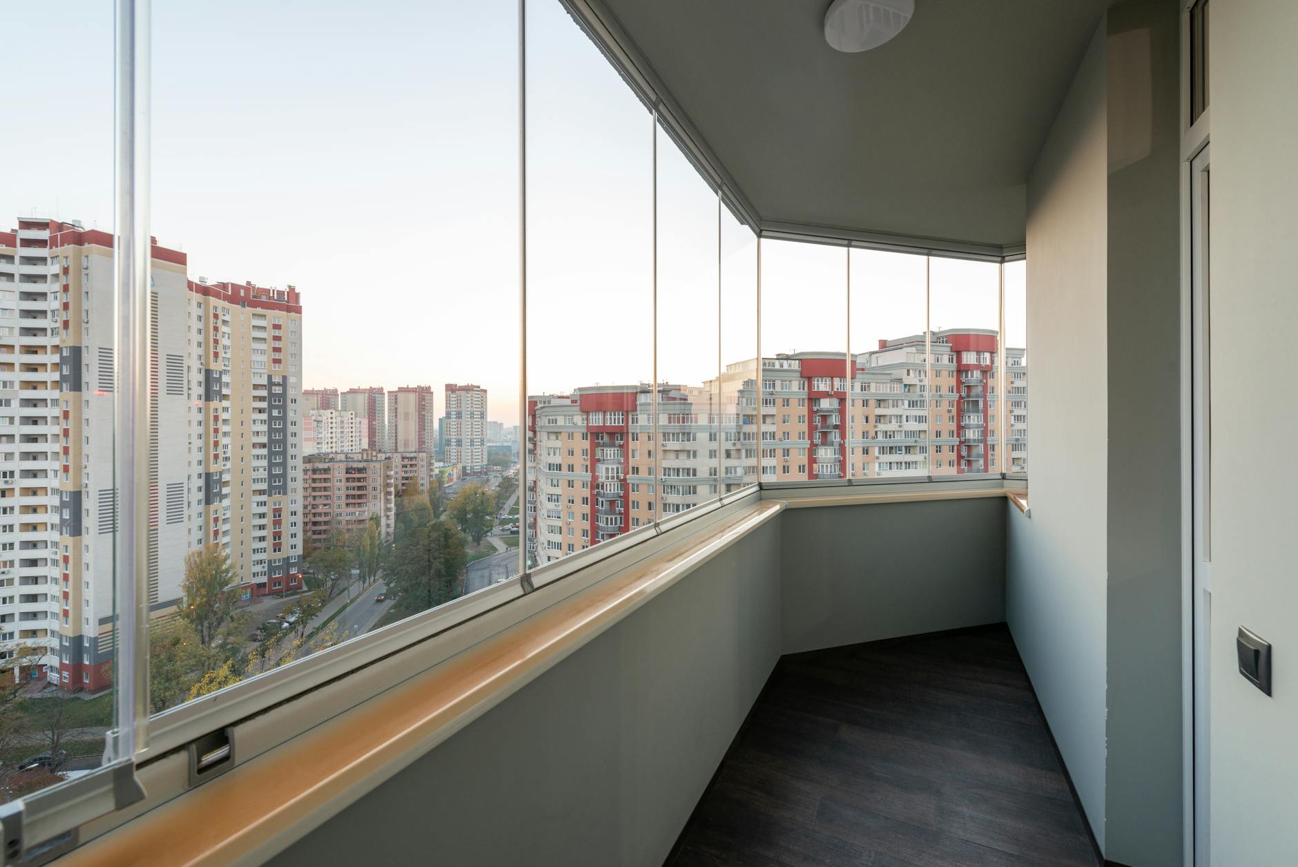 Aviso do IPMA em Lisboa: como proteger casa, janelas e varanda em 15 minutos 9 A modern balcony with glass panels overlooking a city's high-rise buildings at sunset.
