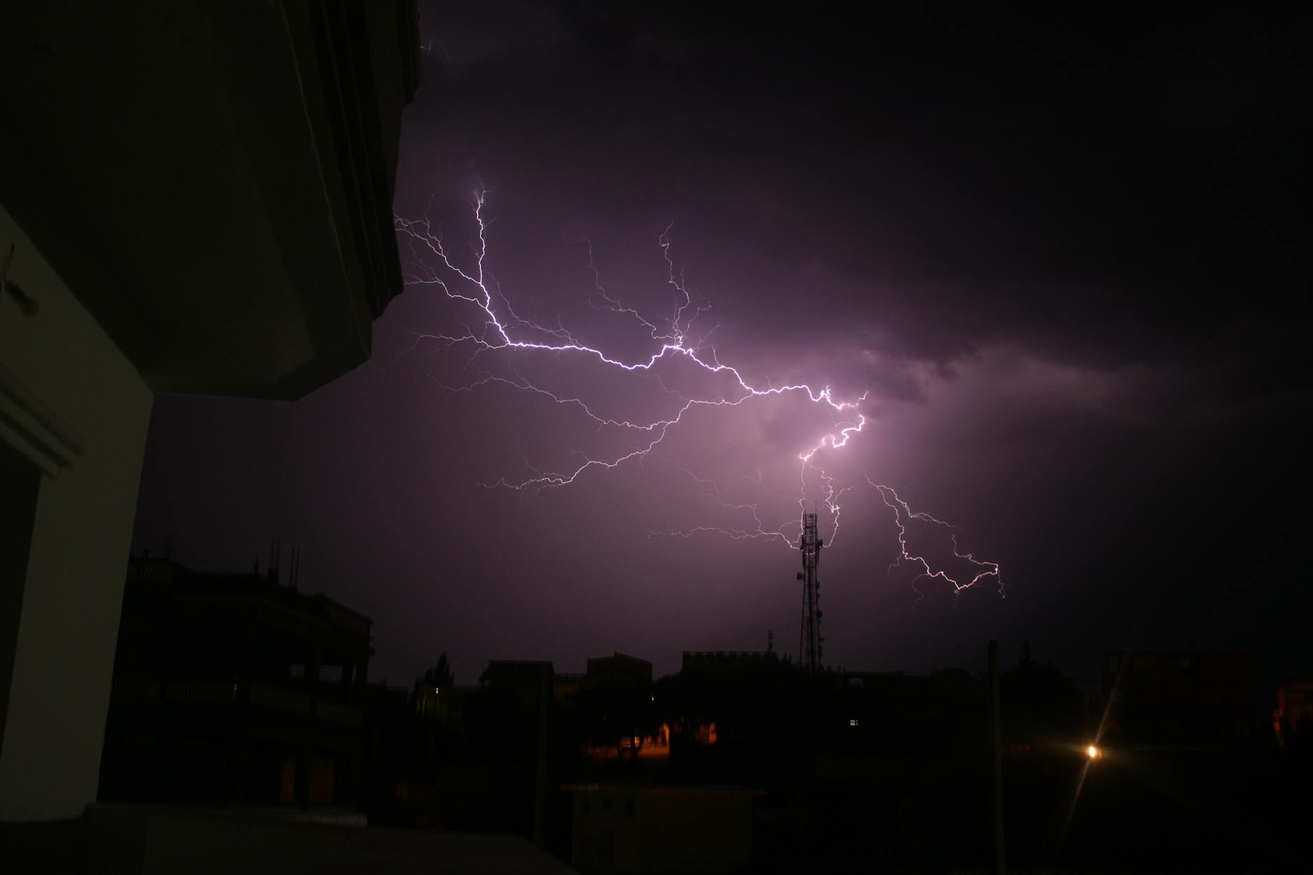 Trovoadas: regras simples para reduzir riscos em casa e na rua 3 A striking lightning storm illuminates the night sky above silhouetted city buildings.