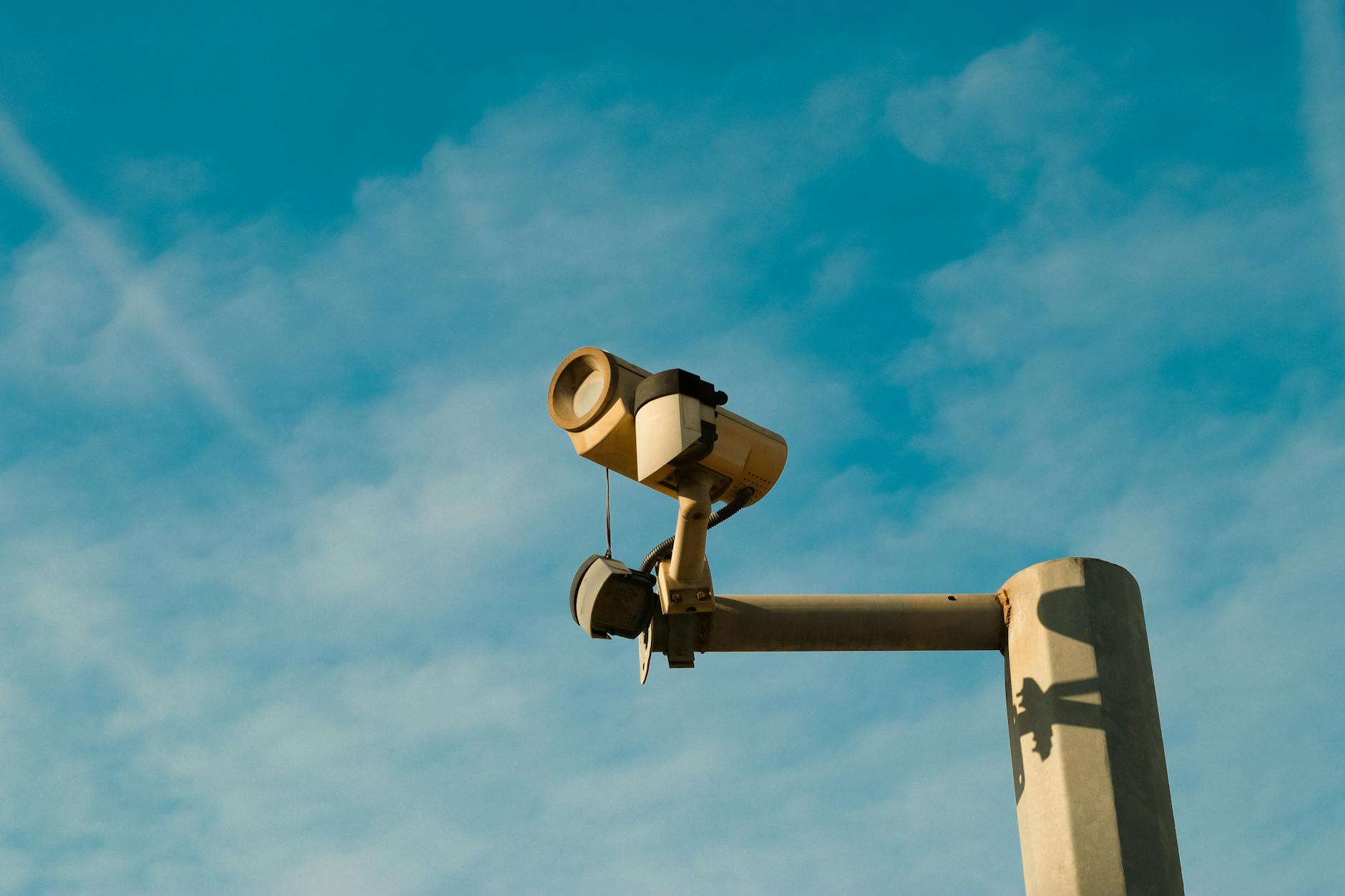 O que verificar antes de viajar com mau tempo: checklist para Lisboa–AML 6 A surveillance camera mounted outdoors against a bright blue sky, symbolizing security and monitoring.