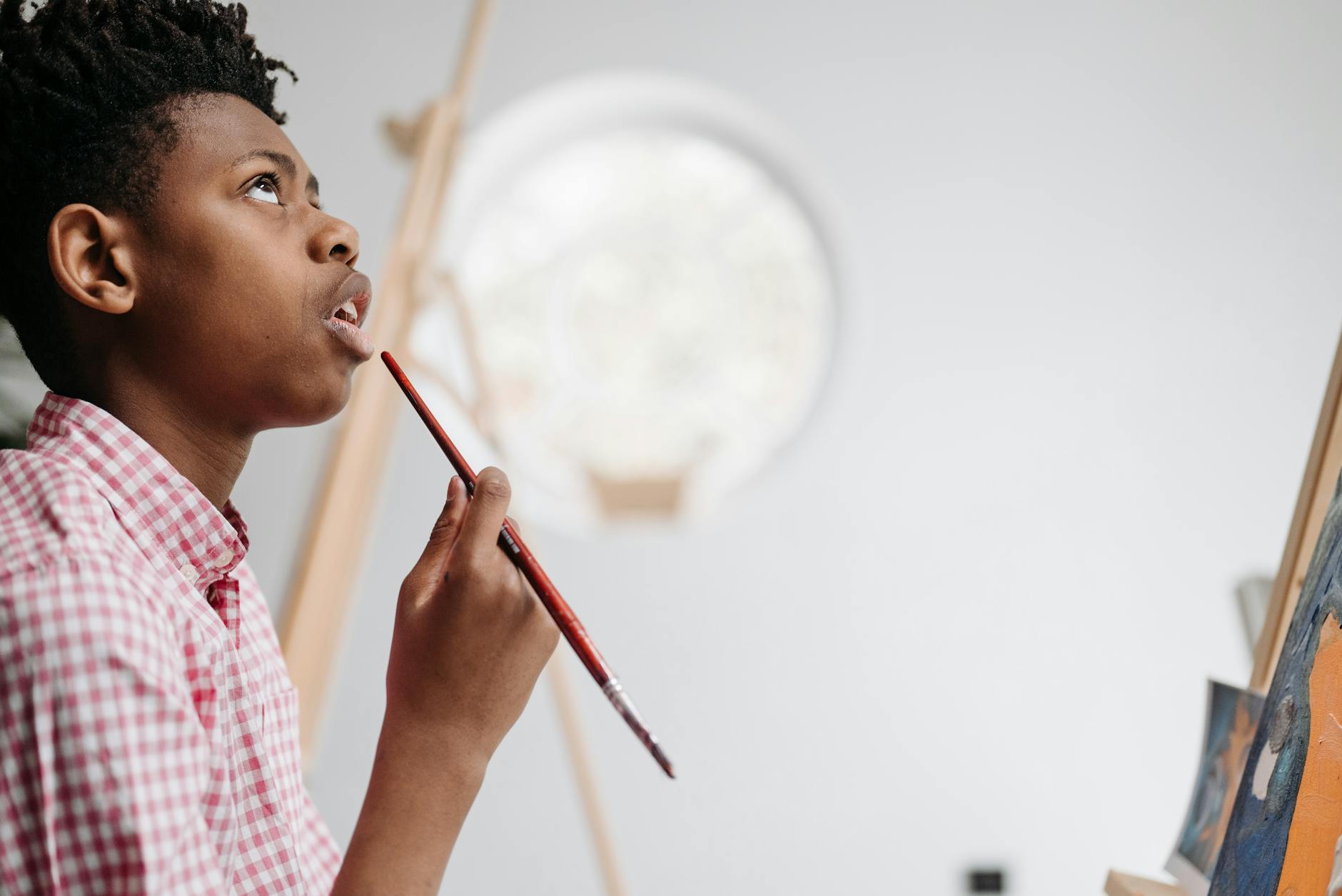 A young boy ponders his next creative stroke with a paintbrush in an art studio.