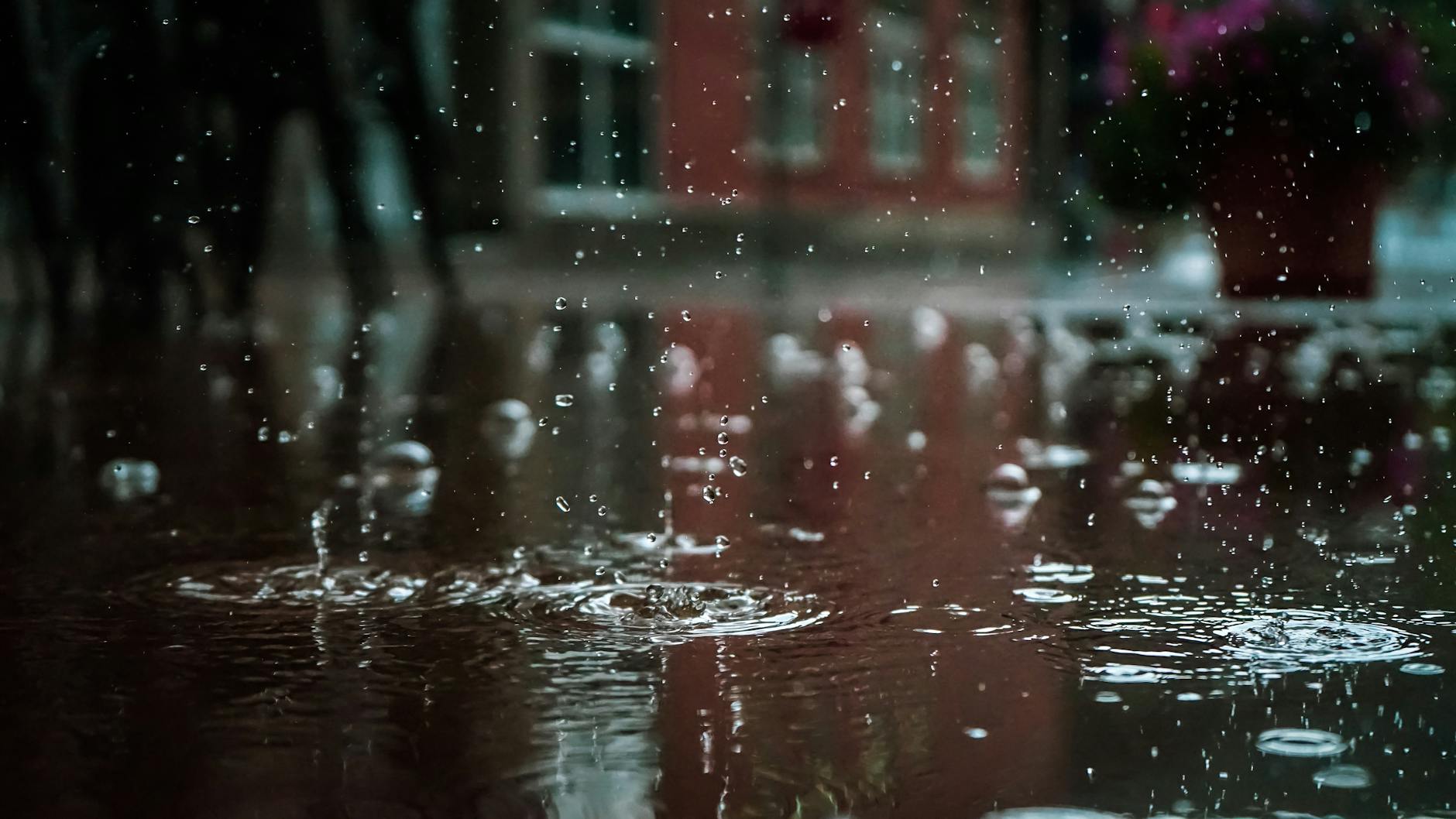 Vai chover forte em Lisboa? Checklist rápido antes de sair de casa 4 Close-up of raindrops splashing into a puddle, capturing reflections and textures in an outdoor urban setting.
