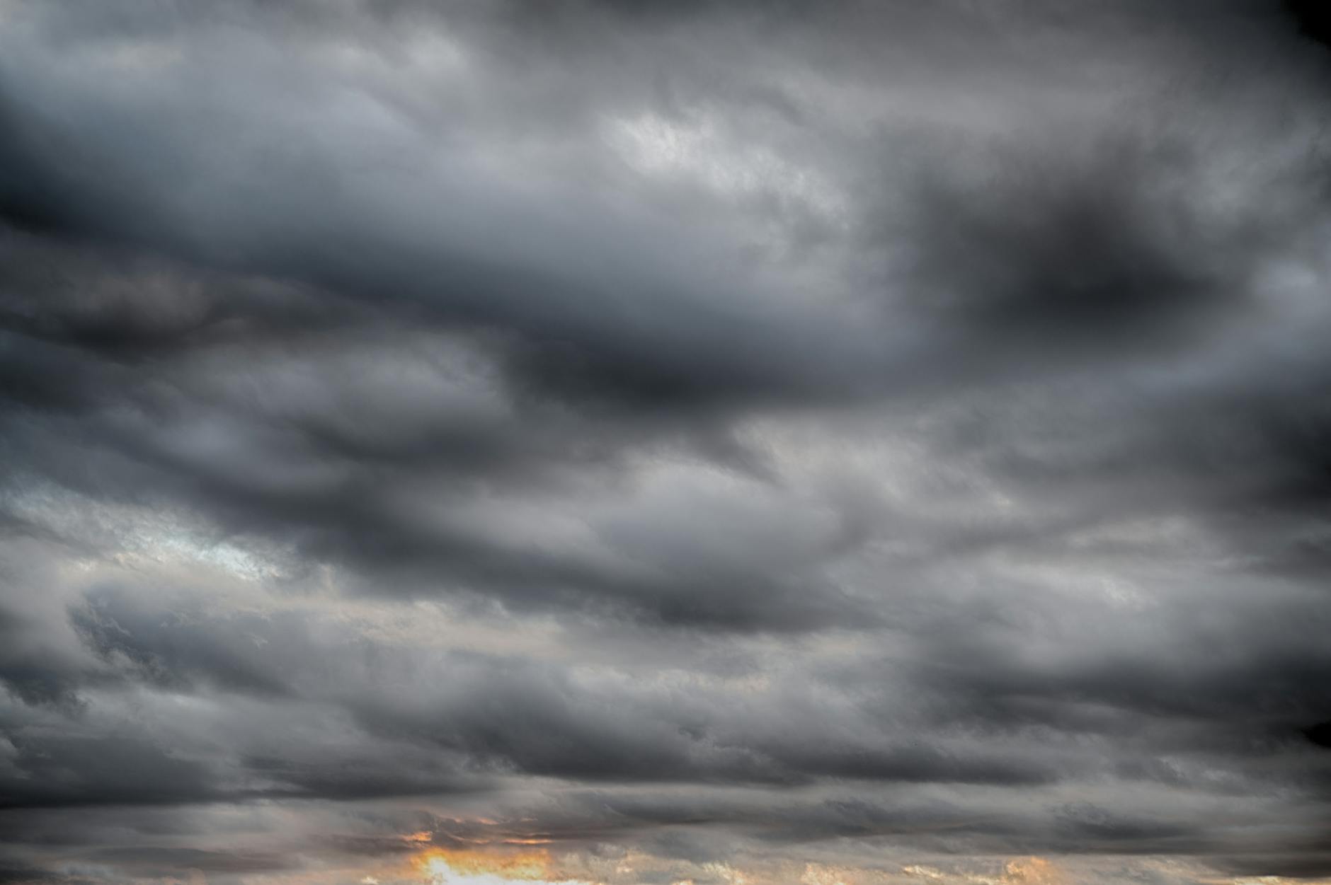 Dark storm clouds loom during a dramatic sunset, hinting at a brewing thunderstorm.
