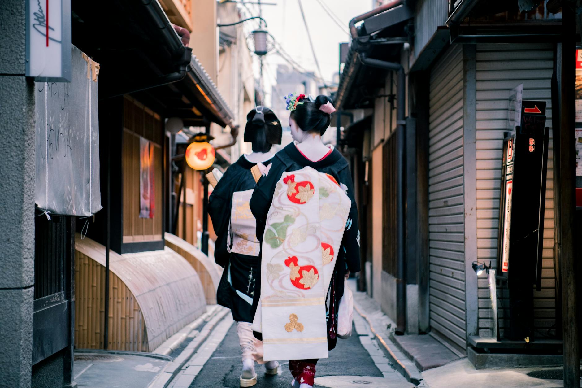 Elegant Japanese women in kimonos walking through a Kyoto alley, showcasing cultural fashion.