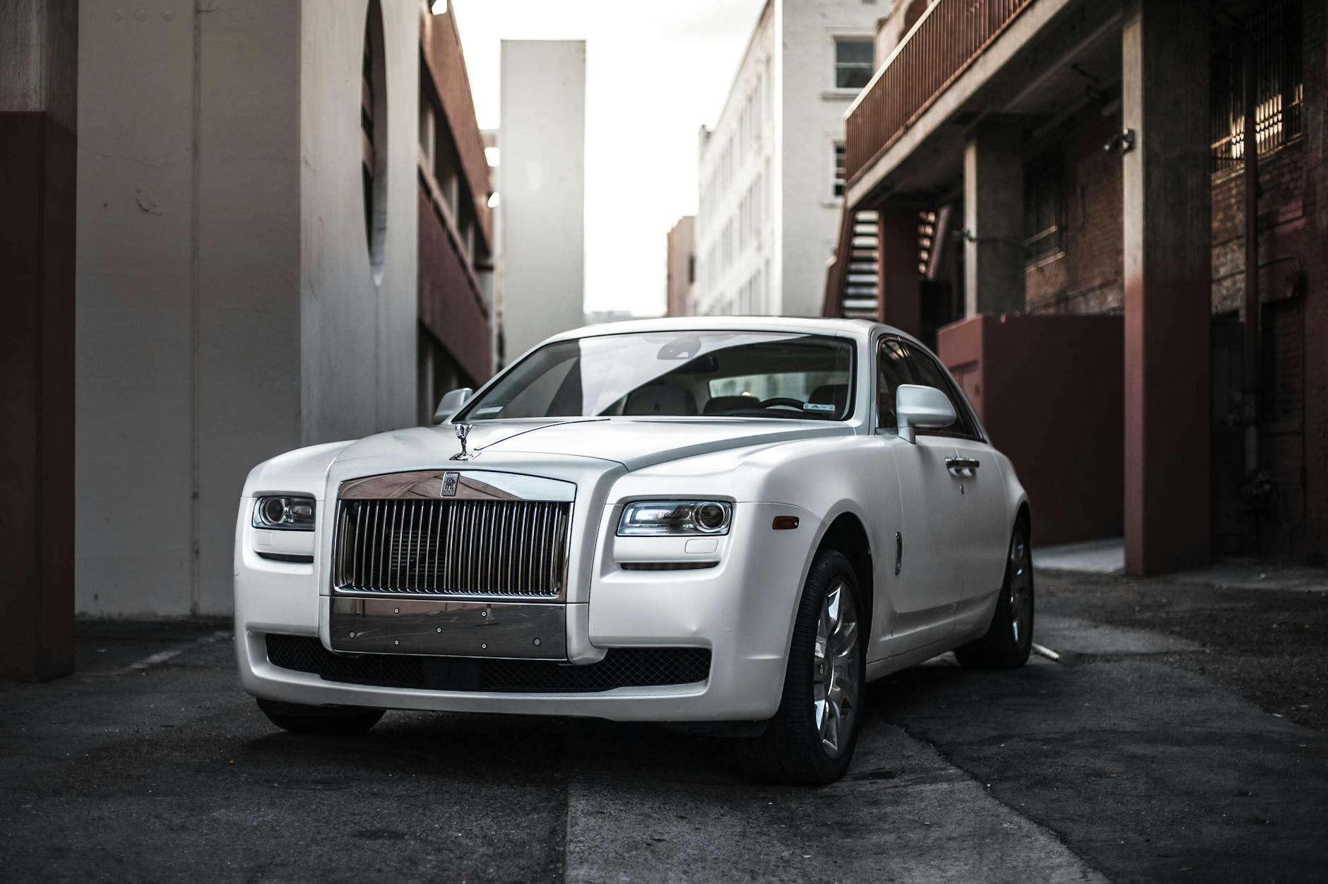 Roteiro “Só Quem Mora Sabe”: Pequenos Segredos De Lisboa 5 Elegant white luxury car parked in an urban alley, exuding sophistication and style.