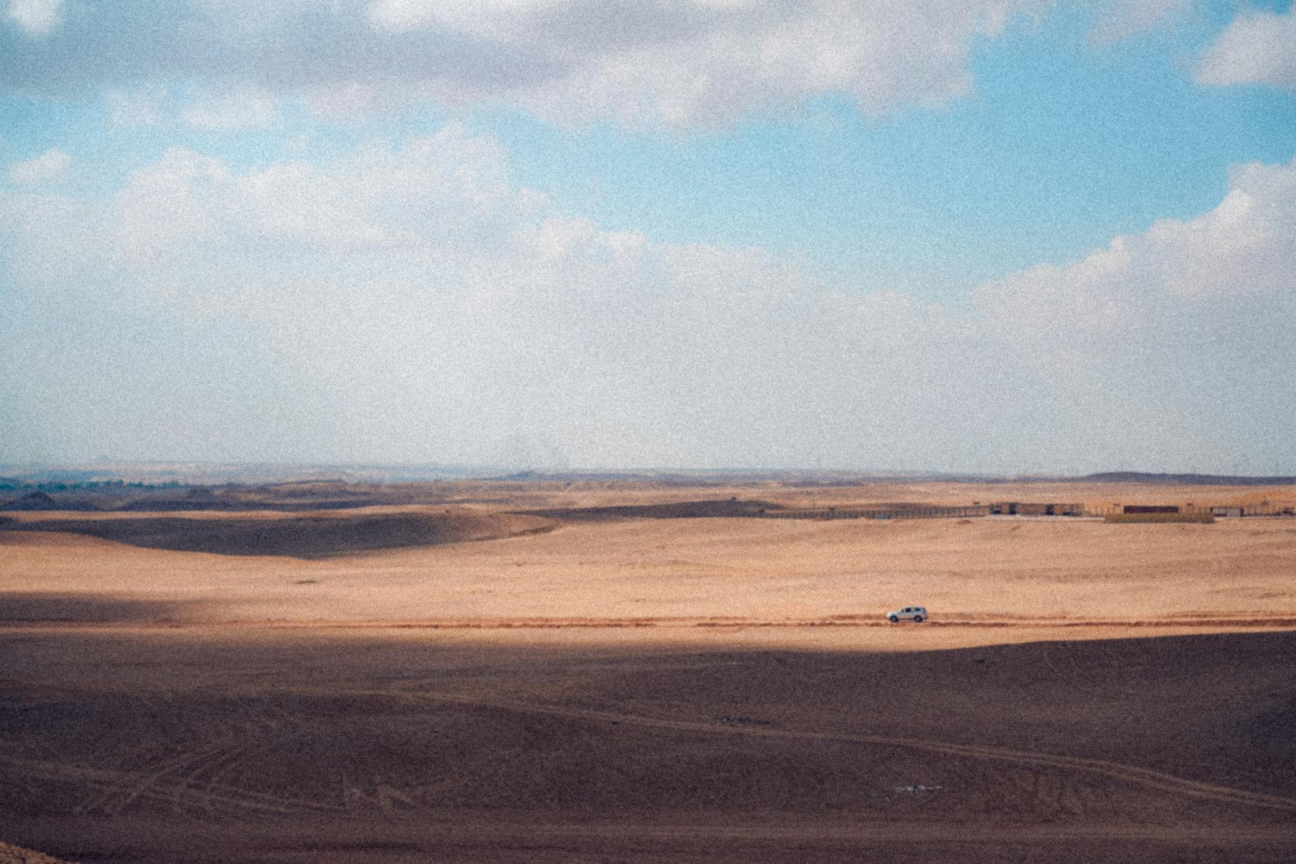 Cheias em Lisboa: como evitar zonas críticas e planear o percurso 7 Expansive desert scene featuring a solitary car under a cloudy blue sky.