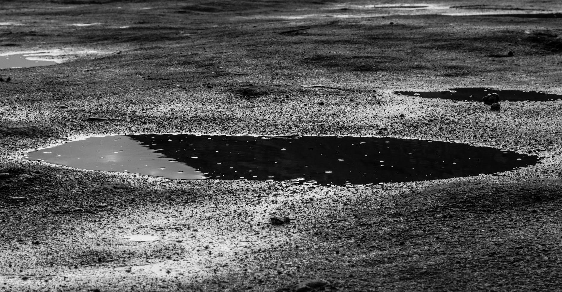 IC19 e A5 em dias de chuva: erros típicos e como conduzir com margem 4 Monochrome image of puddles on a wet surface, showcasing texture and reflection.