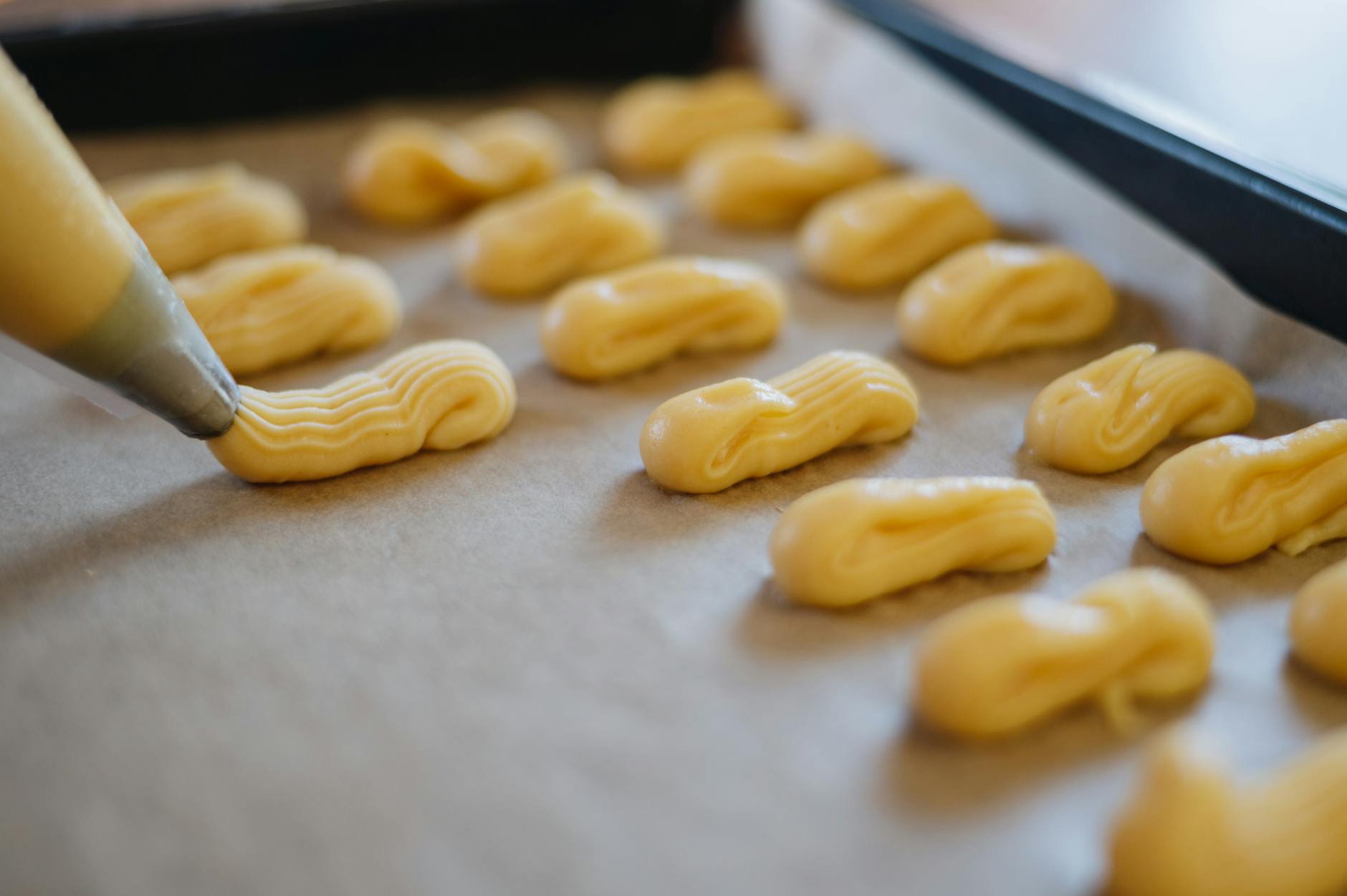 Pastry bag piping dough onto a baking sheet for eclairs preparation. Close-up food photography.
