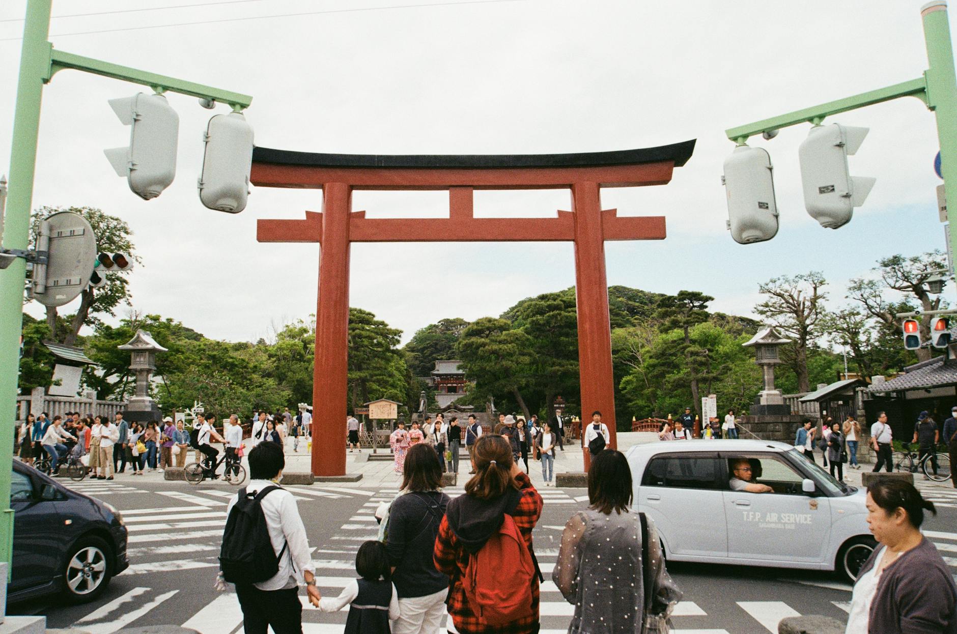 People crossing at a busy intersection under a large red torii gate in Kamakura, Japan.