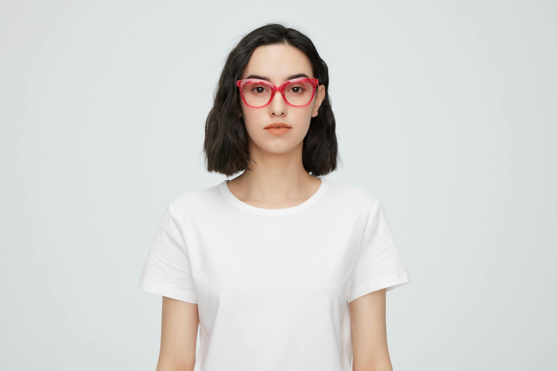 ModaLisboa: Como Ver O Melhor Sem Ser “Do Meio” 2 Portrait of a young woman wearing red eyeglasses and a white shirt against a plain background.