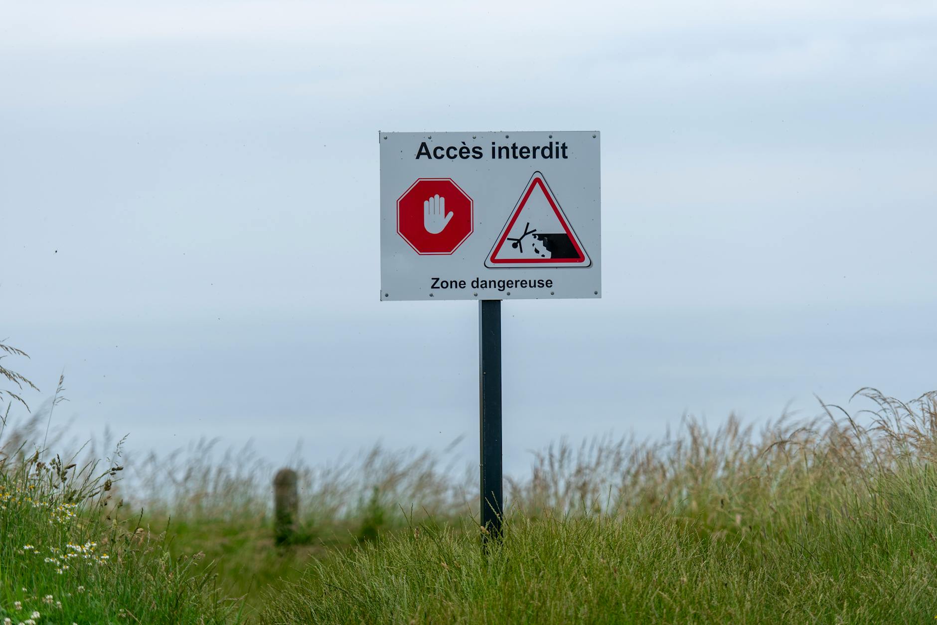 Sign saying 'Accès Interdit' in a grassy area, warning of a dangerous zone.
