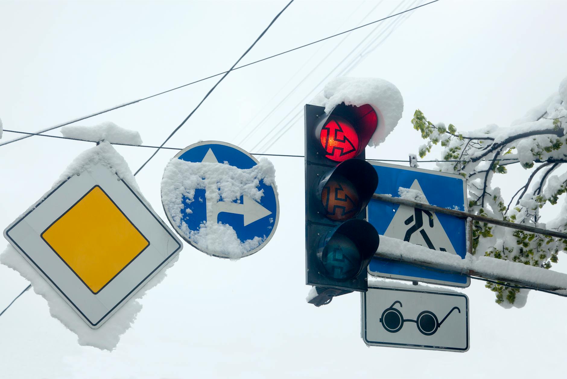 Desvios de trânsito: causas mais comuns em Lisboa e o que fazer na hora 2 Snow-covered traffic light and signs, signaling a winter day with snowflakes.