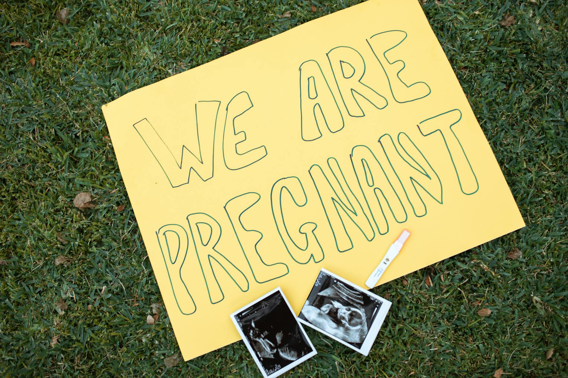 A pé em Lisboa com alerta do IPMA: rotas mais protegidas, erros comuns e o que levar contigo 9 Yellow sign with 'We Are Pregnant' text beside ultrasound images and test on grass.