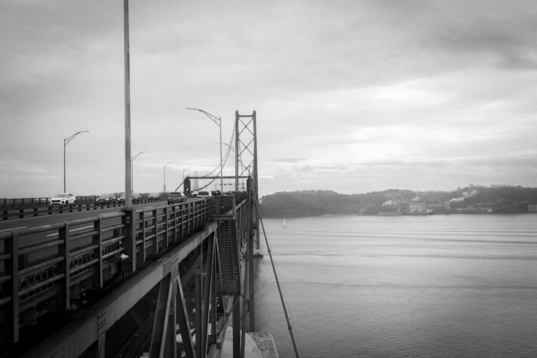 A black and white view of Ponte 25 de Abril bridge in Lisbon, Portugal, overlooking the river.