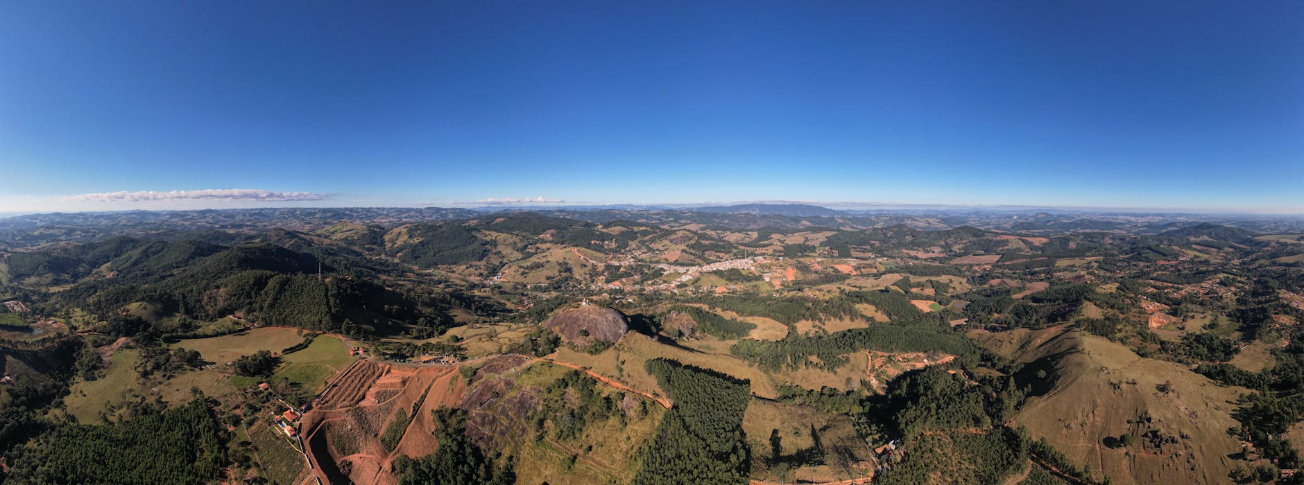 A breathtaking aerial view of Pedra Bela, SP, Brazil showcasing rolling hills and lush greenery under clear blue skies.