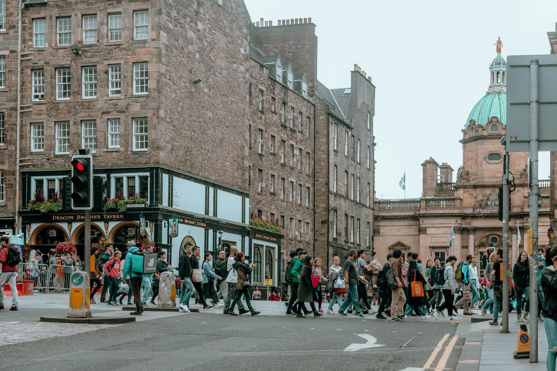 A bustling crosswalk in Edinburgh with a view of Deacon Brodie's Tavern and historic architecture.