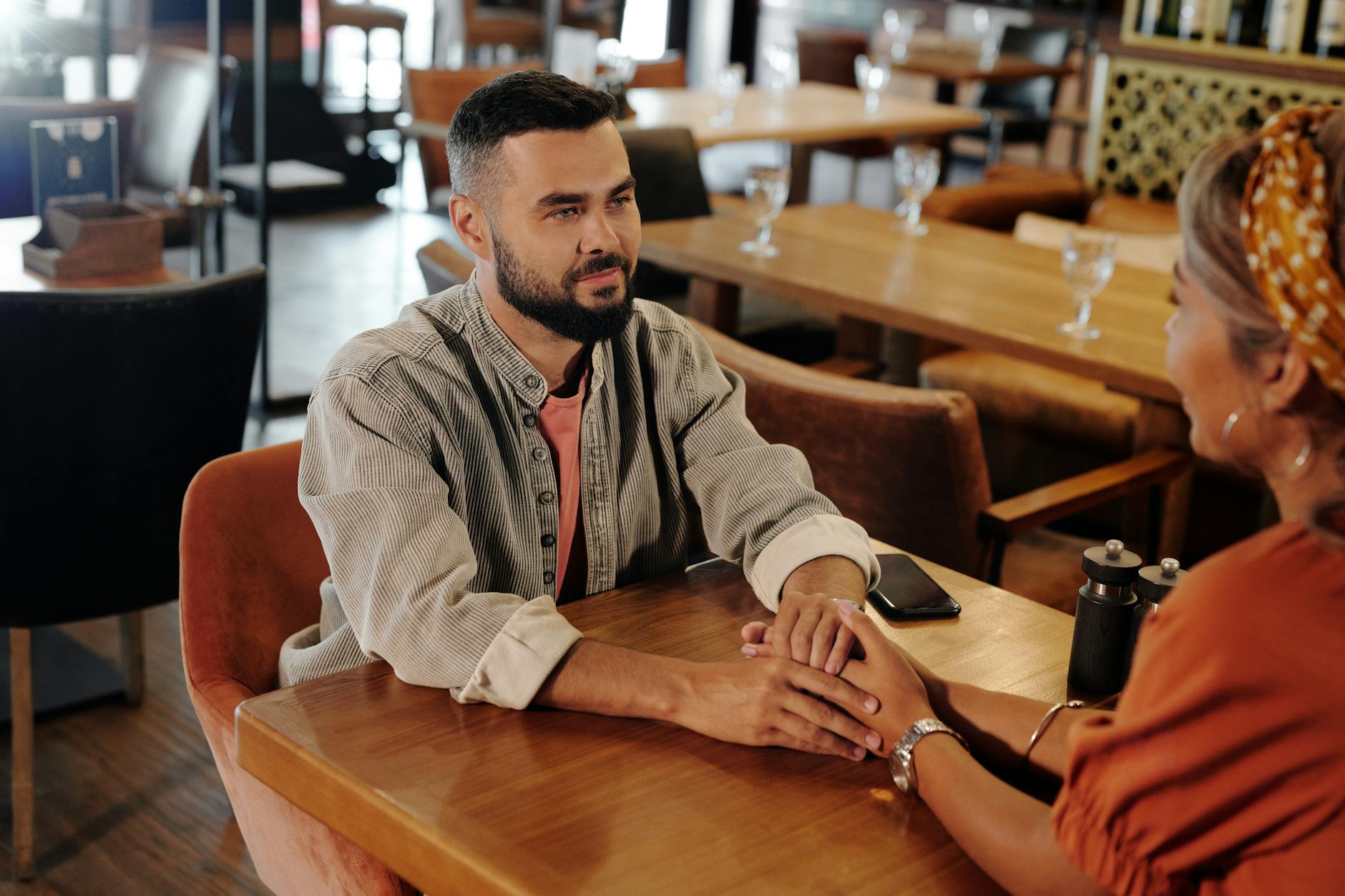 A couple enjoys a romantic moment holding hands at a cozy café, creating a warm atmosphere.