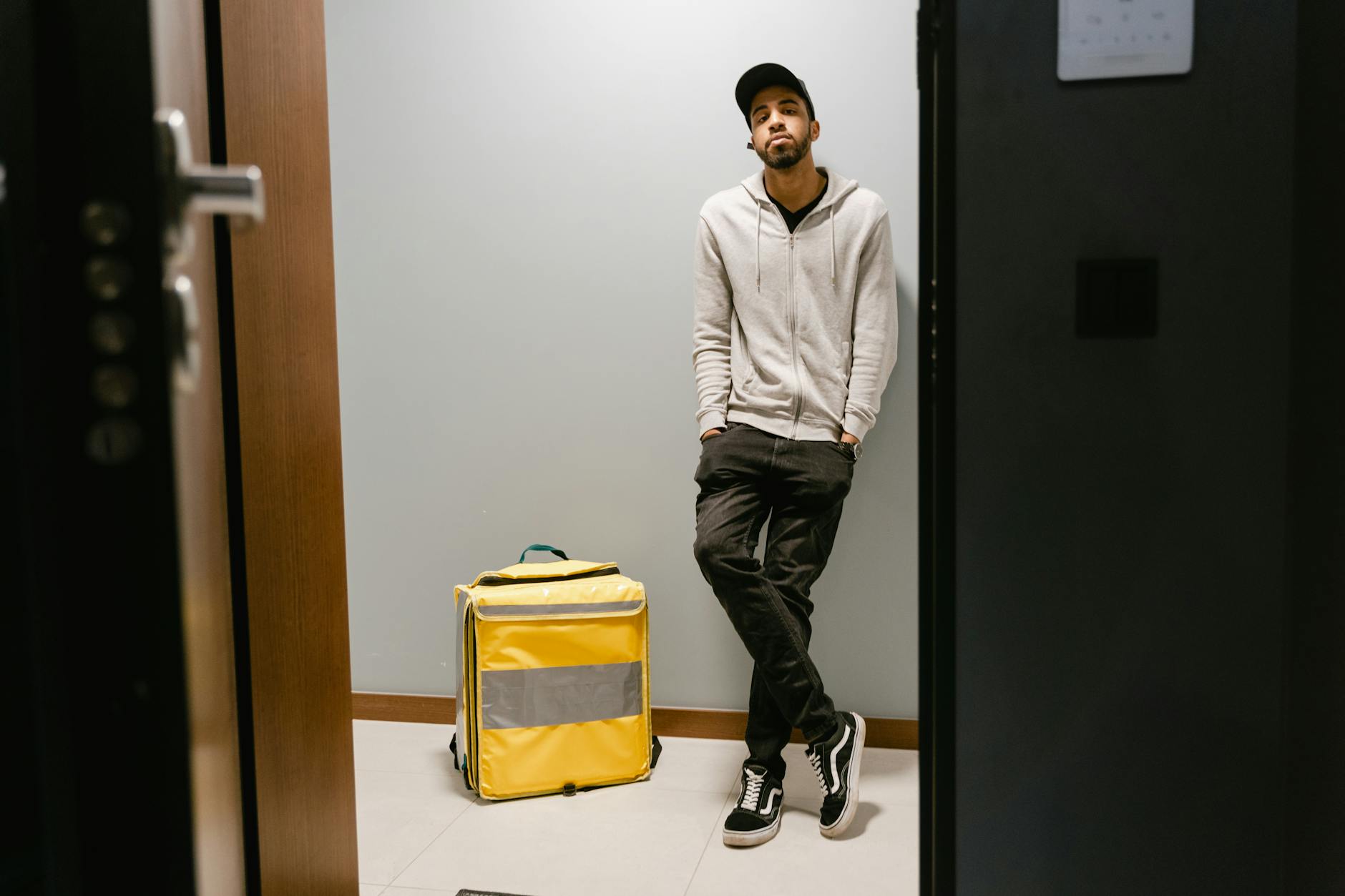 A courier waits by an open door with a yellow food delivery bag, ready to deliver.