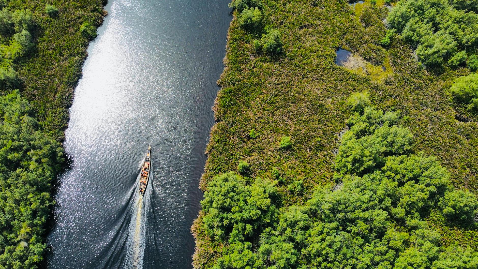 A drone captures a canoe navigating a lush river in Ghana's Volta Region.