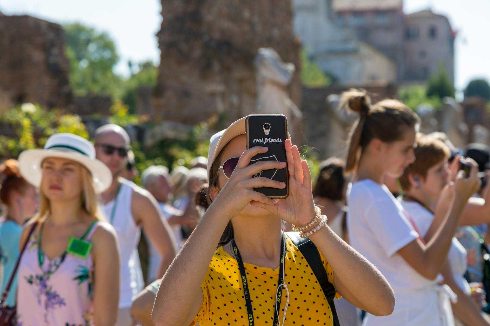 A group of tourists using smartphones to photograph historical ruins on a sunny day.