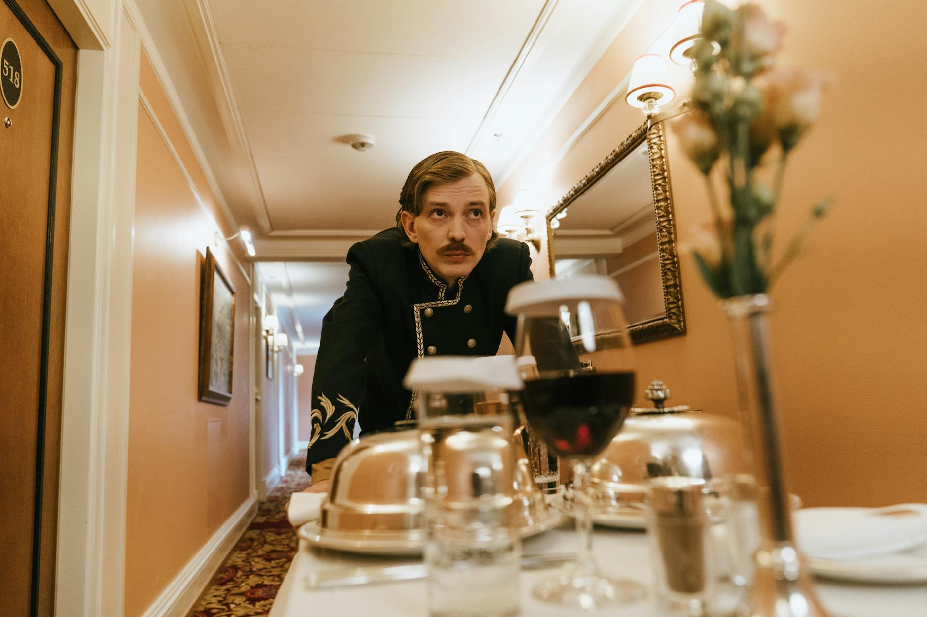 A hotel staff member in uniform delivering room service in an elegant hallway.