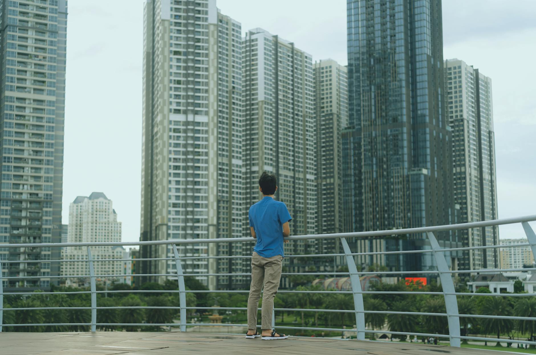 A man stands on a terrace, viewing the modern skyscrapers of Ho Chi Minh City.