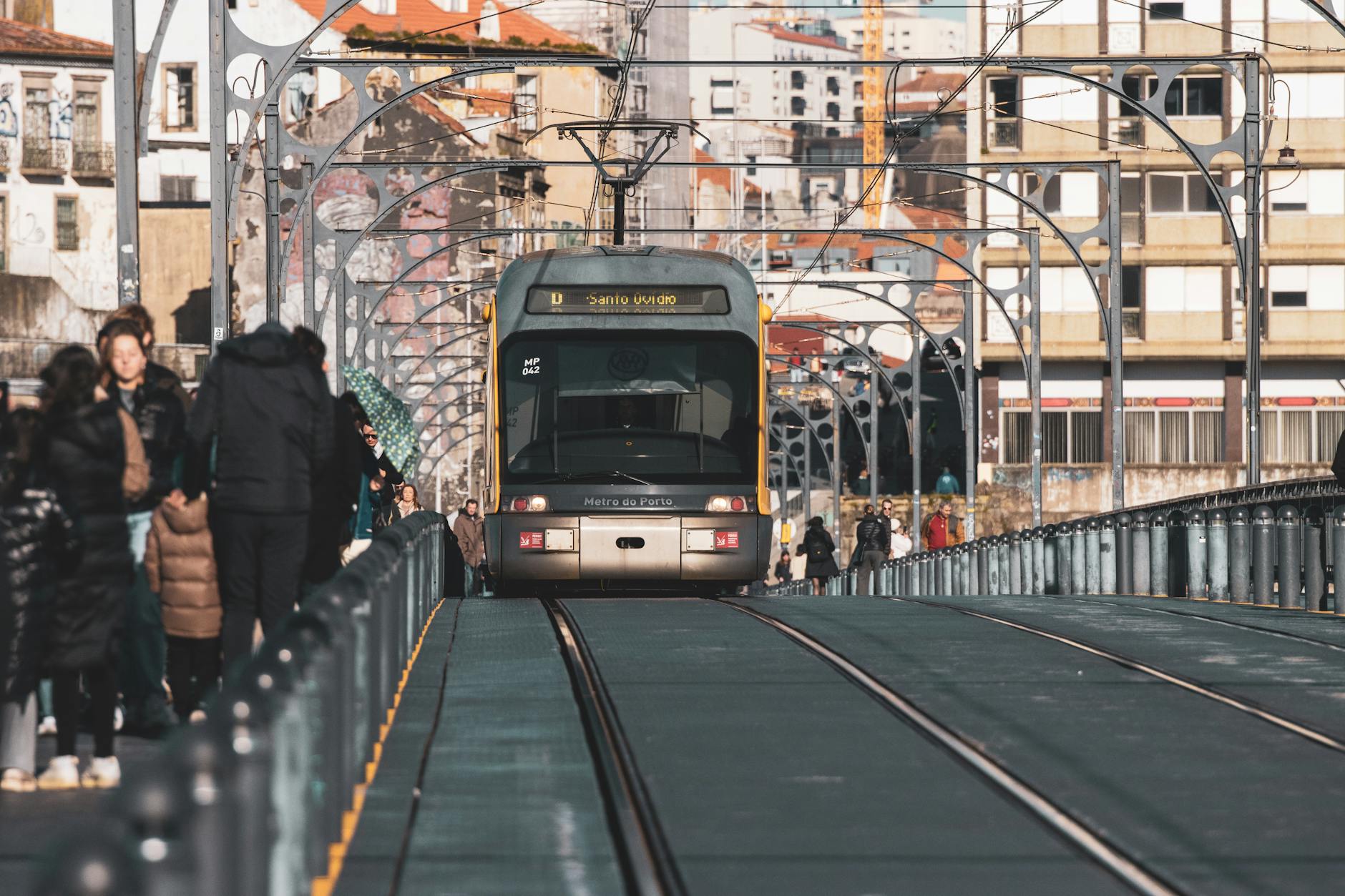A metro tram traveling on the Ponte Luís I Bridge in Porto, Portugal, surrounded by urban architecture.