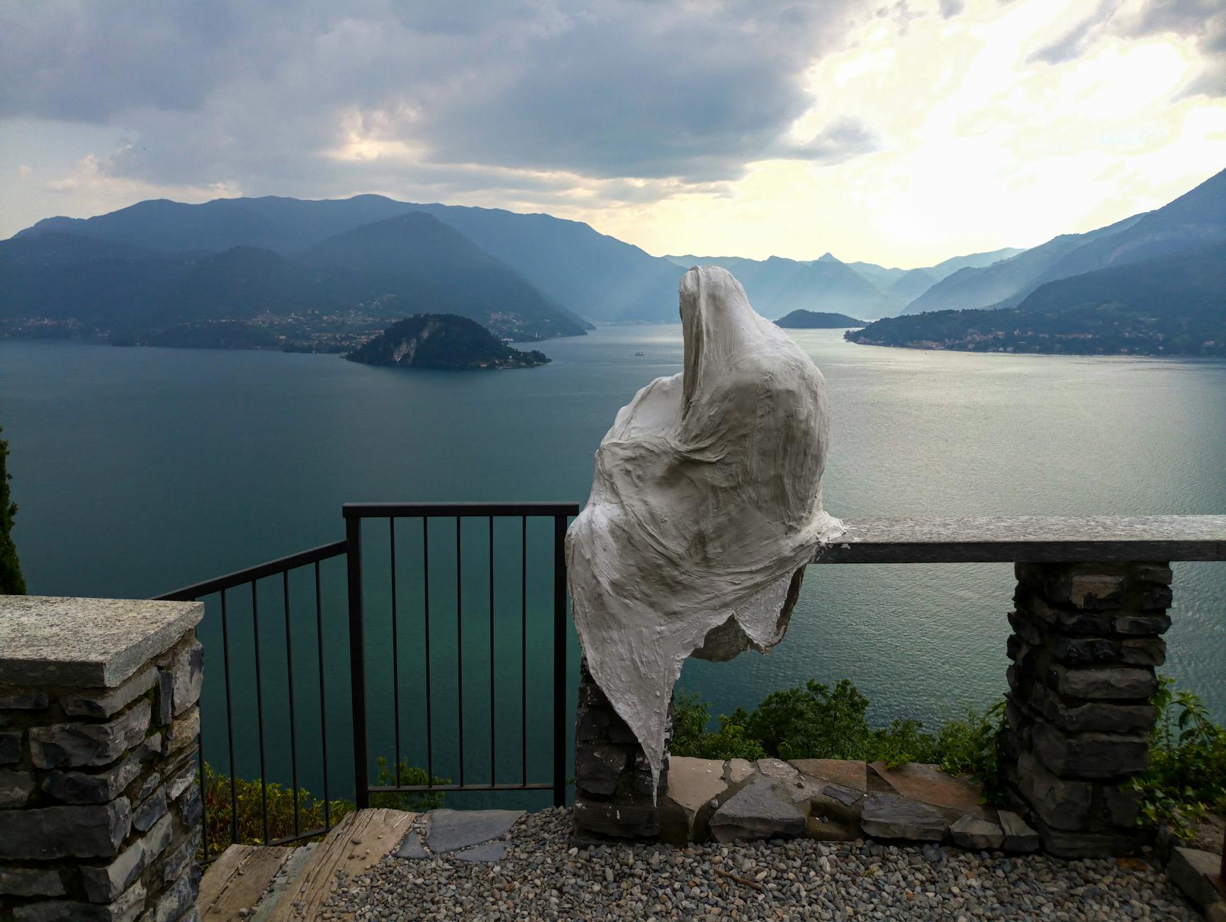 A mysterious sculpture gazes over Lake Como in Lombardia, Italy, surrounded by serene mountain views.