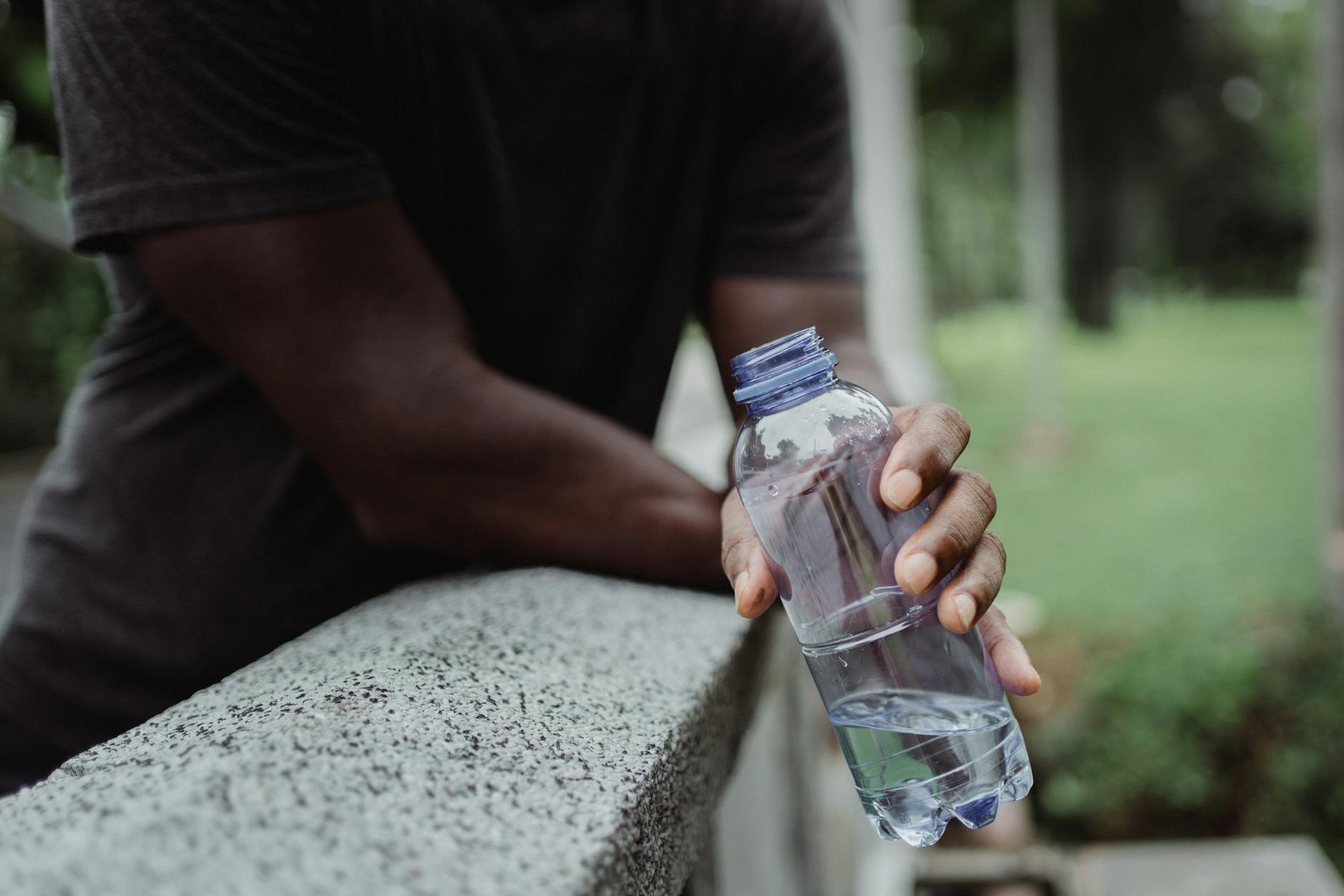 NOS Alive: “ir com calor” — como não estragar o festival por causa do tempo 6 A person holds a plastic water bottle on a concrete rail outdoors, emphasizing hydration.