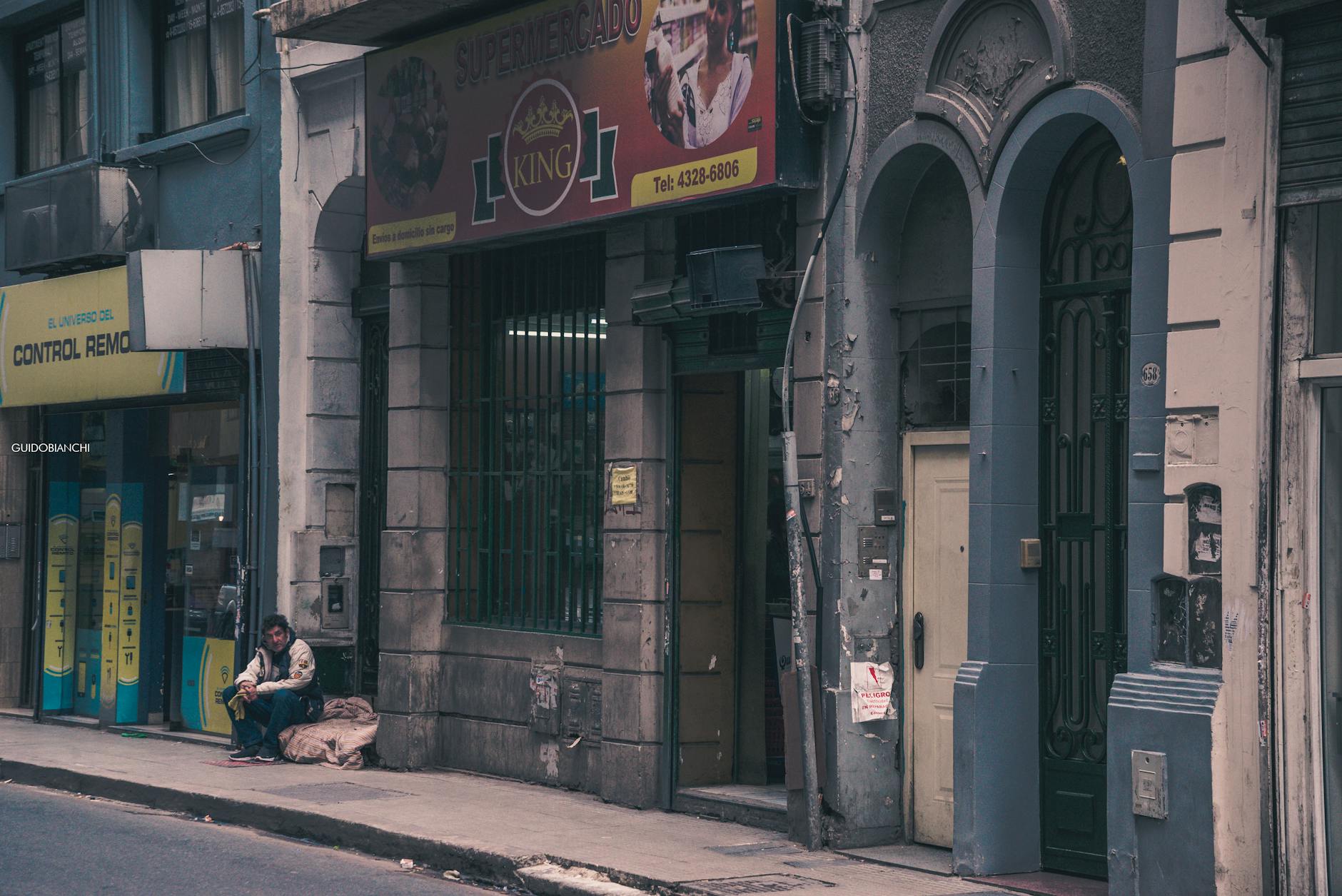 A person sits outside on an urban street near old buildings and shops.