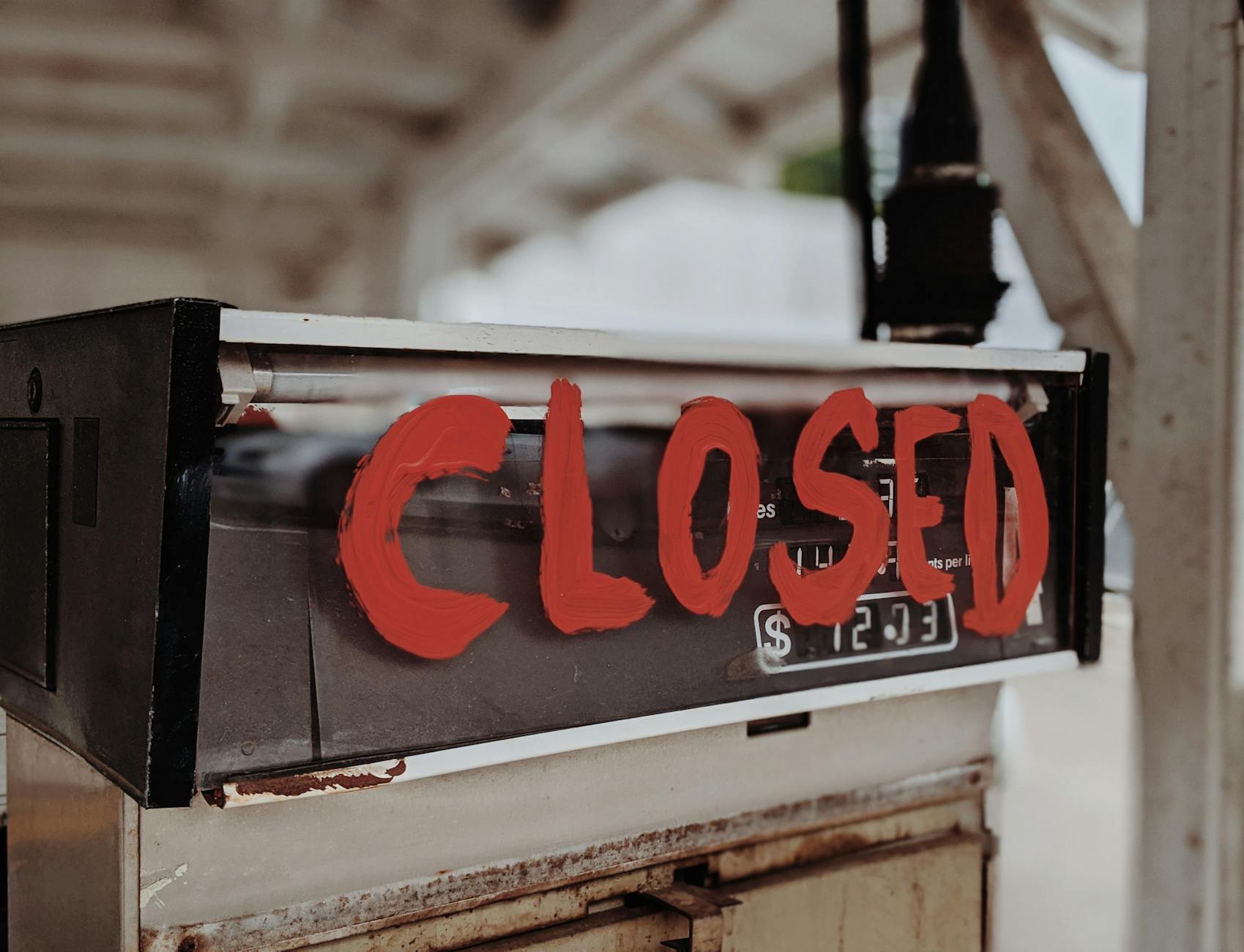 A red 'CLOSED' sign painted on an old gas pump at an outdoor station.