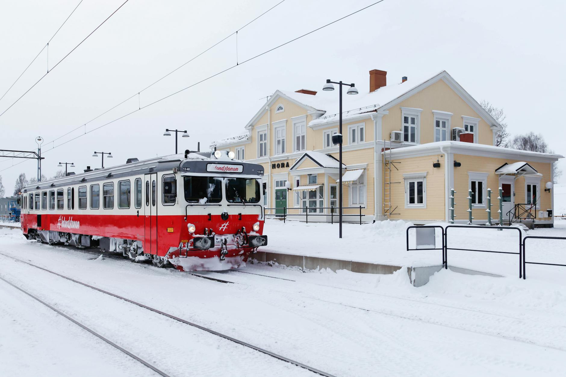 A red train at Mora Station in a snowy winter landscape, Sweden.