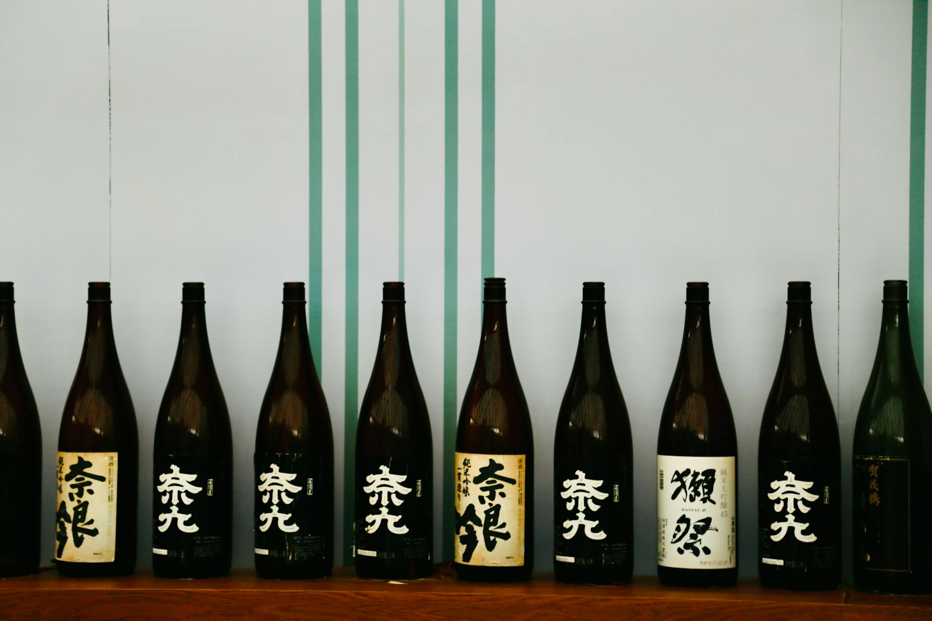 A row of Japanese sake bottles displayed on a wooden shelf against a decorative backdrop.