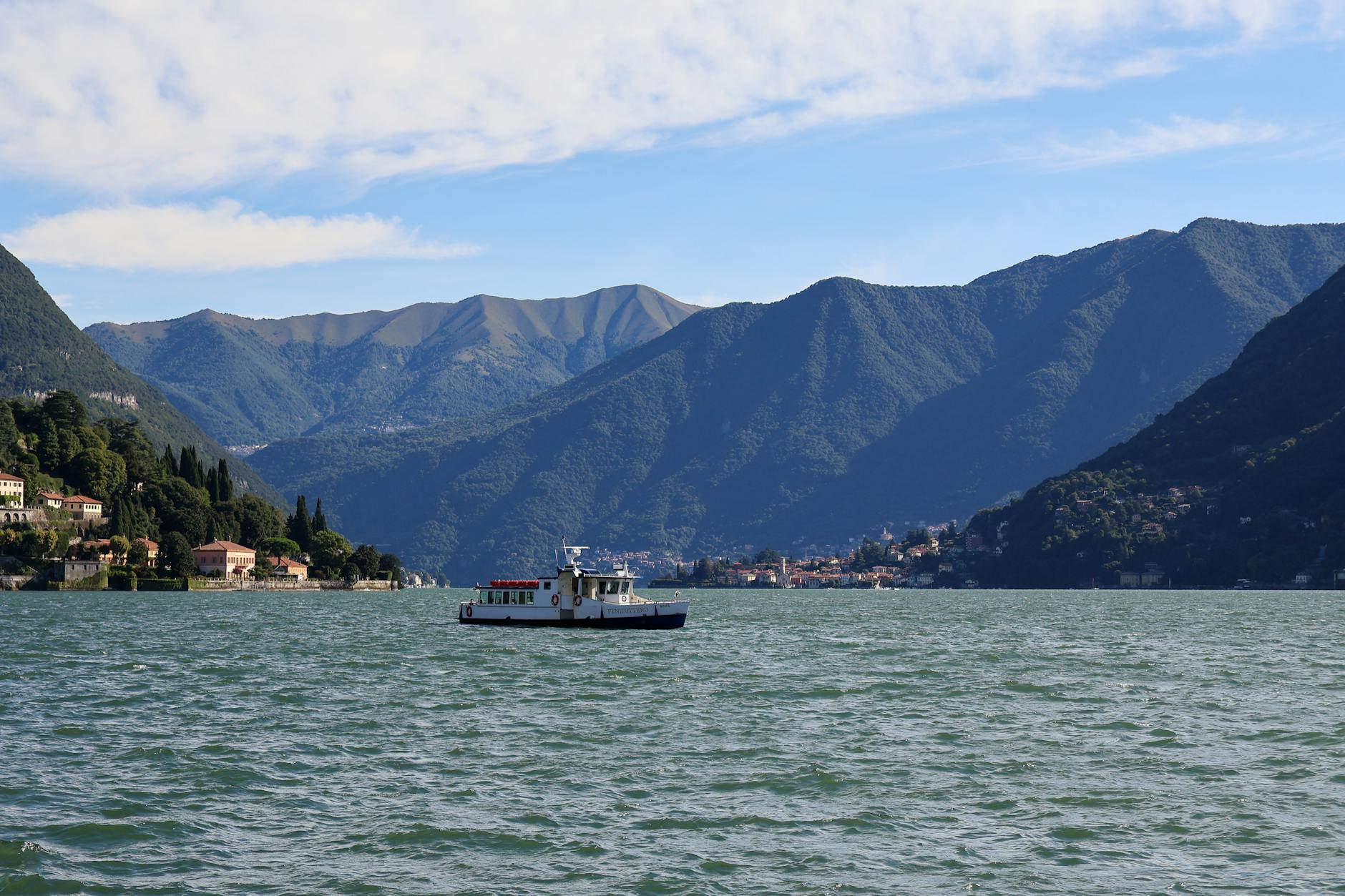 A serene view of Lake Como with a ferry boat and mountains in the background.