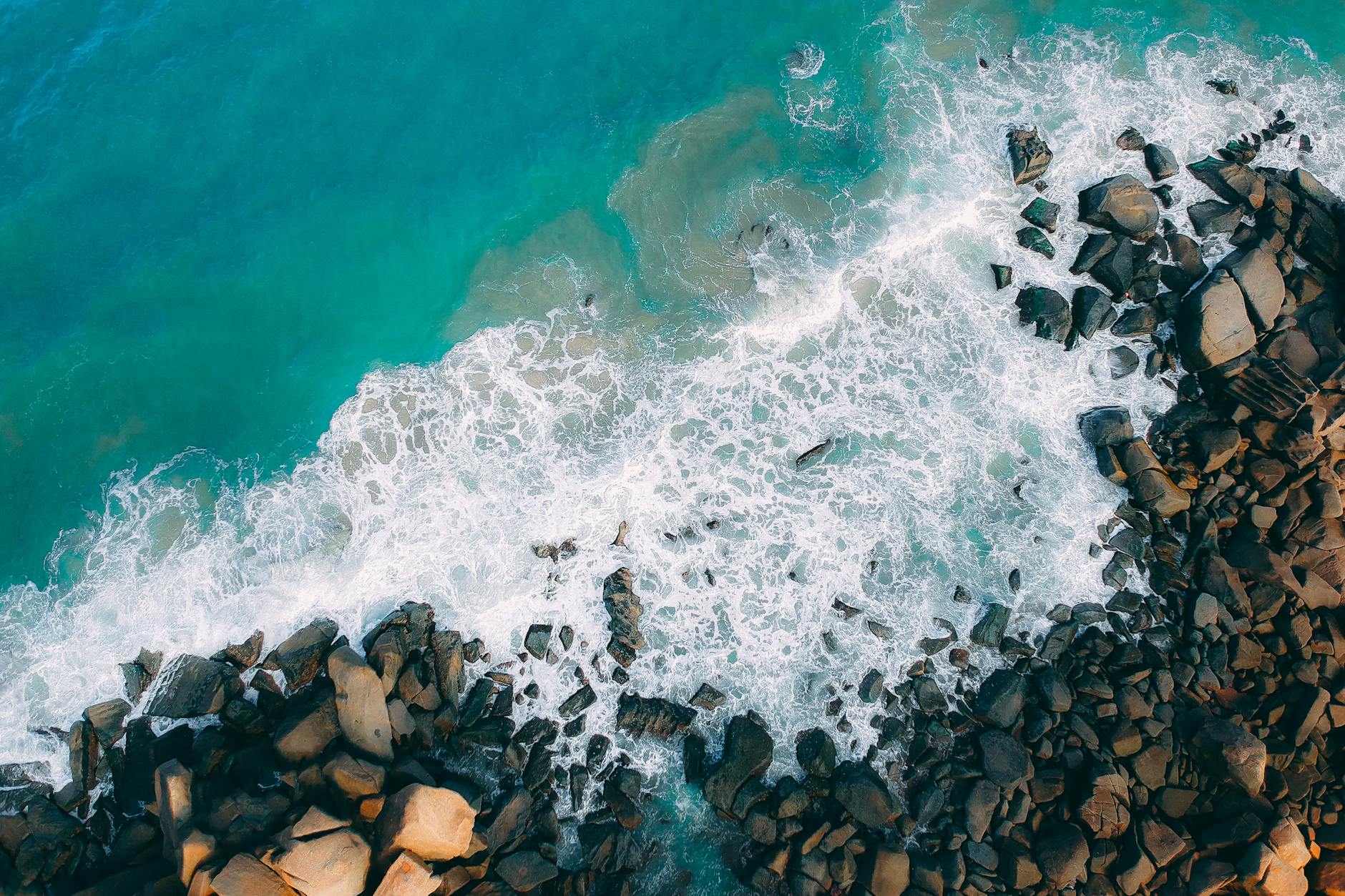 A stunning aerial view of ocean waves crashing on a rocky shore, capturing nature's raw beauty.
