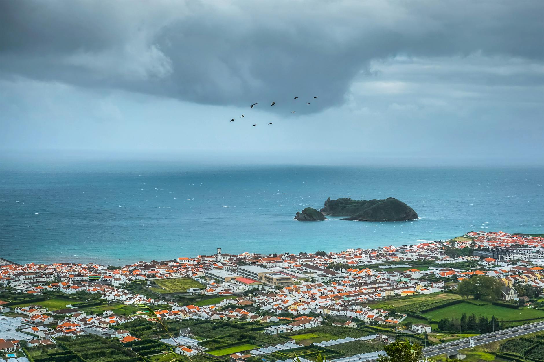 A stunning aerial view over Vila Franca do Campo and the Atlantic Ocean with dramatic clouds.