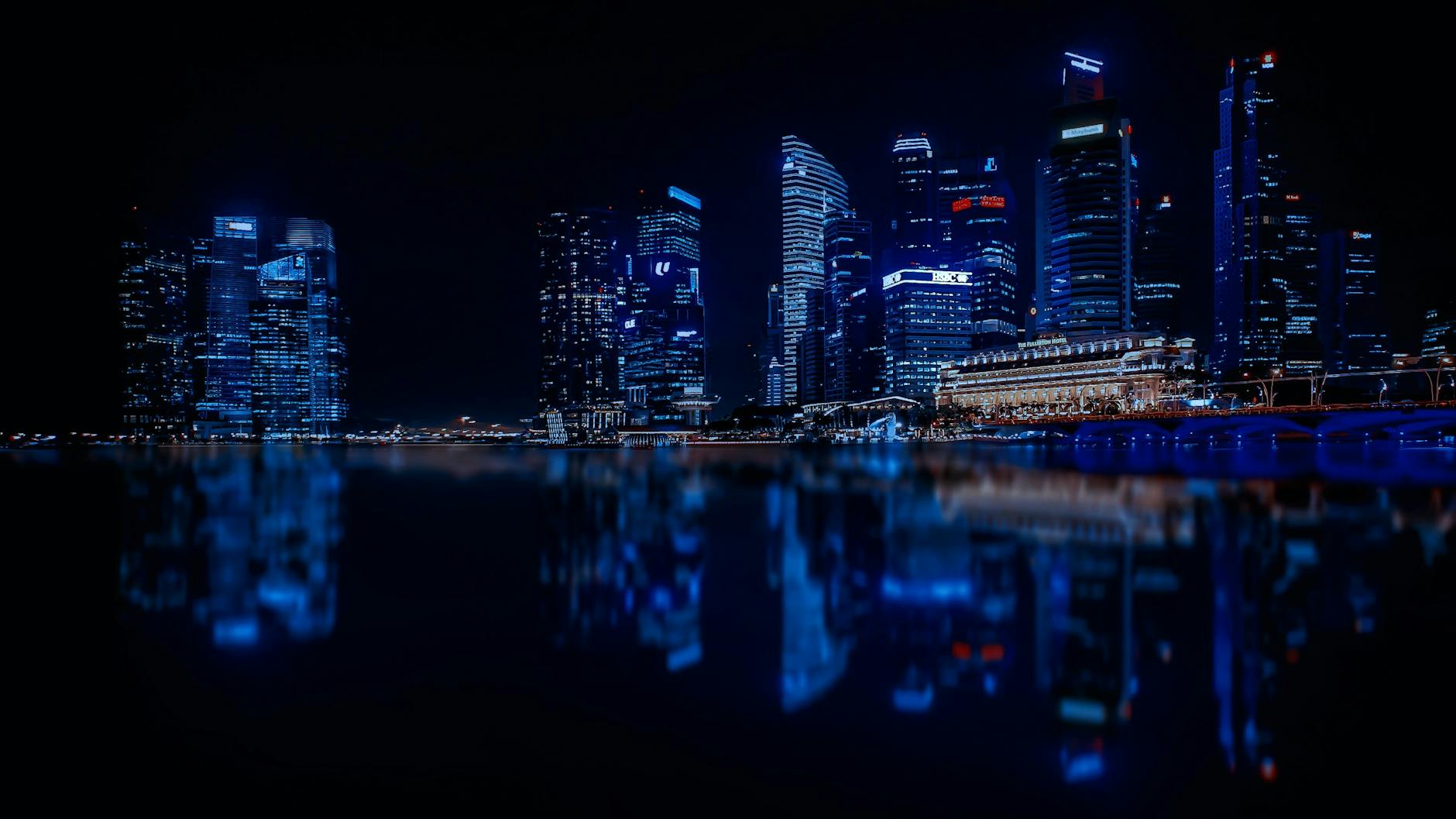A stunning night view of a city skyline with illuminated skyscrapers reflecting on calm water.