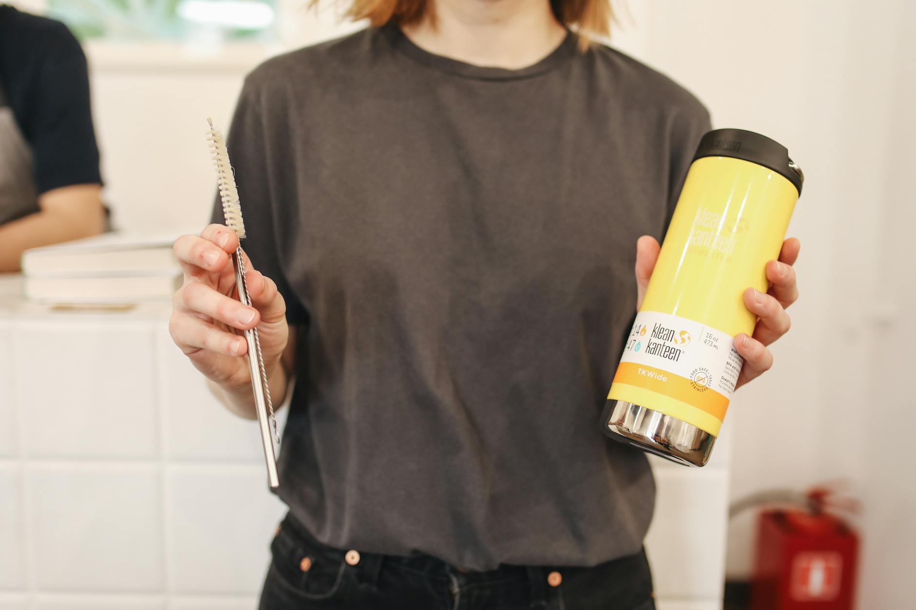 A woman holds a reusable thermos and metal straw, promoting zero waste lifestyle.