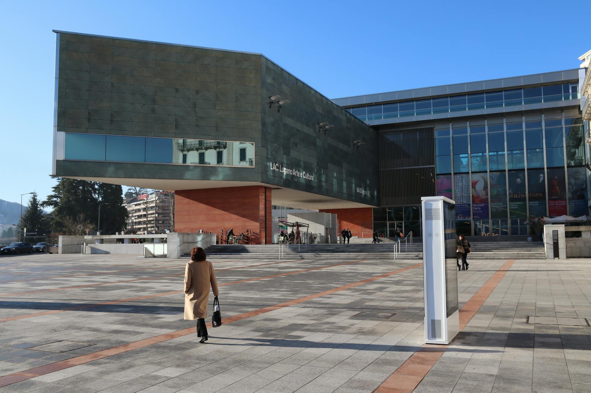 A woman walks towards the LAC Lugano Arte e Cultura in Switzerland on a sunny day.
