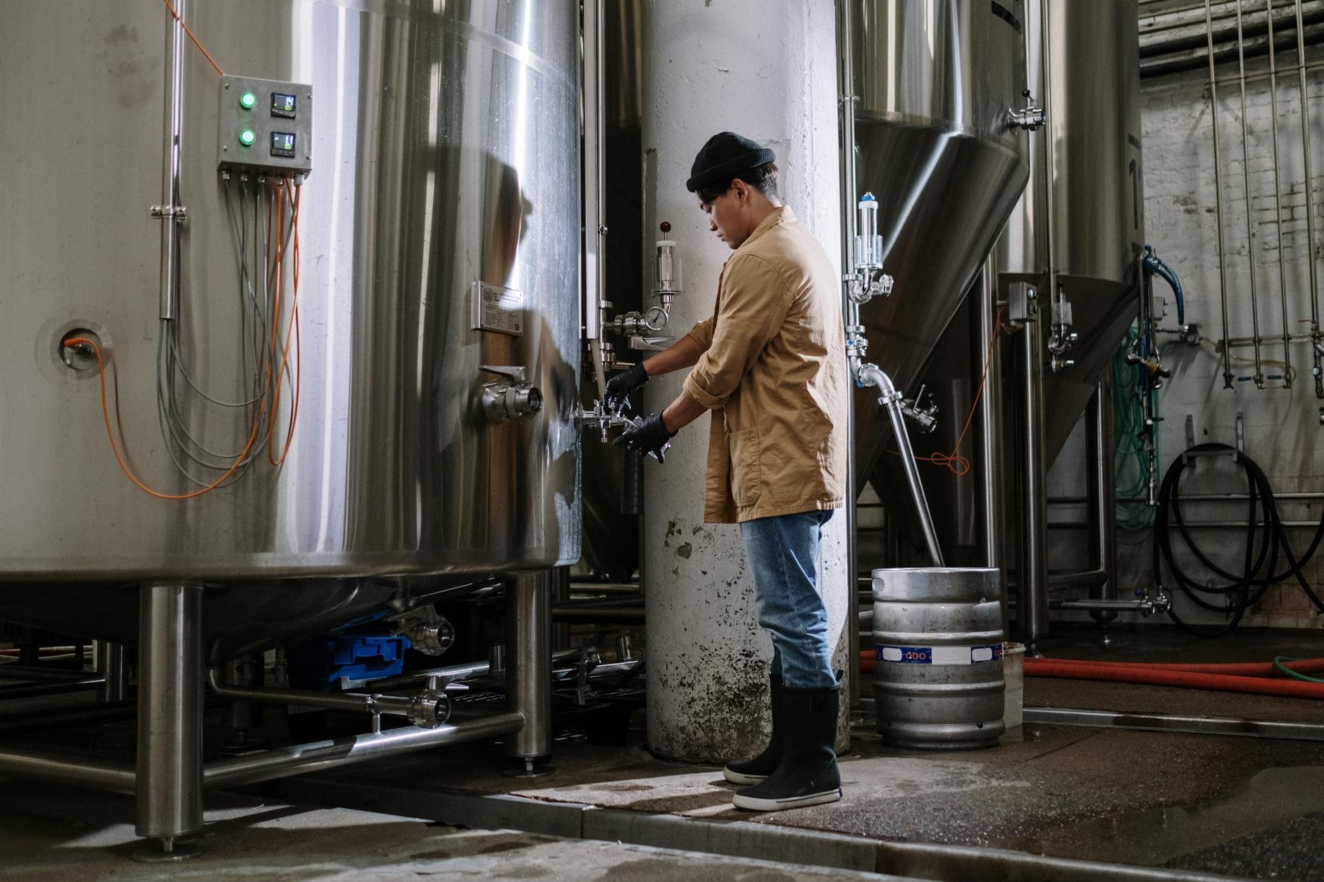 Asian brewmaster working with large stainless steel fermentation tanks in a brewery.