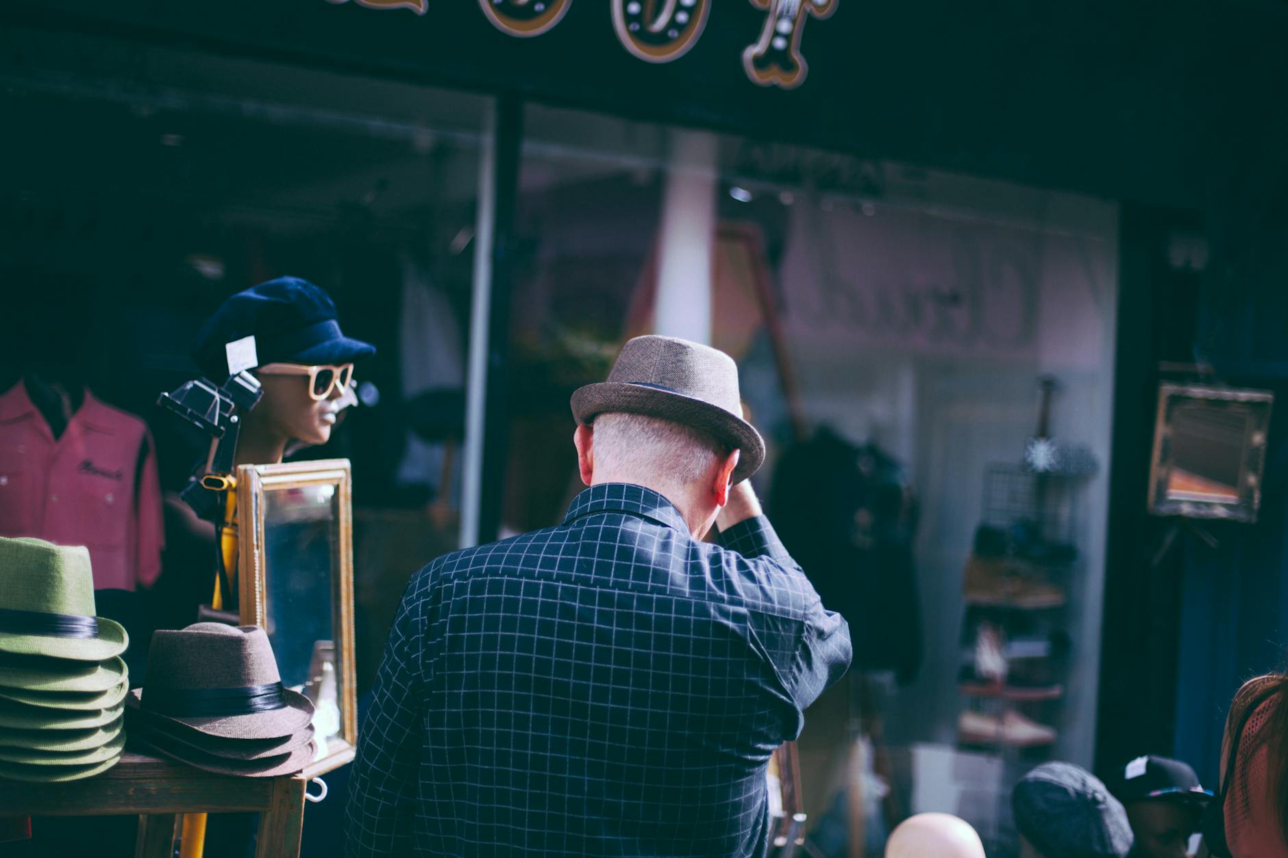 Back view of a man browsing hats at a street market stall on a sunny day.