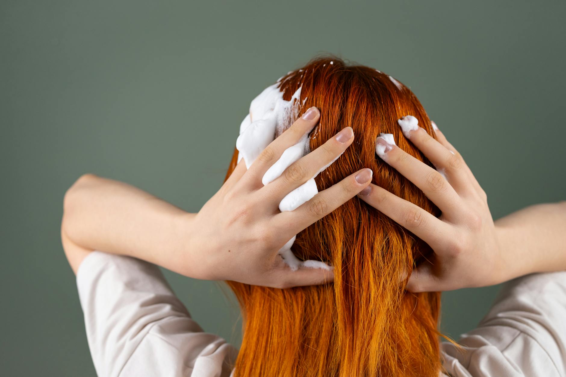 Back view of person washing red hair with shampoo in studio setting.