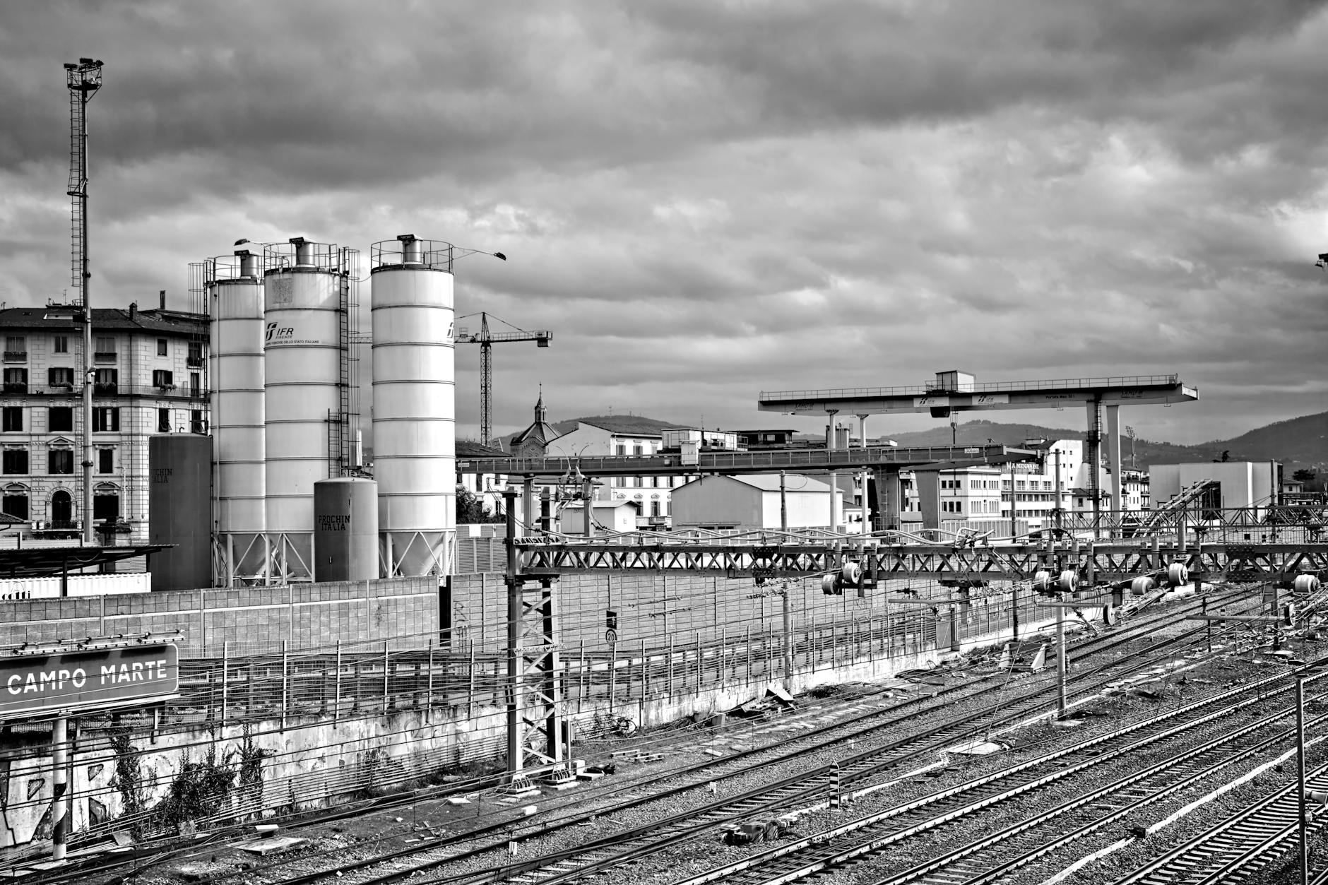 Campo Novo vs EntreCampos: qual vai parecer “bairro a sério” primeiro 4 Black and white urban scene depicting a railway yard and industrial buildings under an overcast sky.