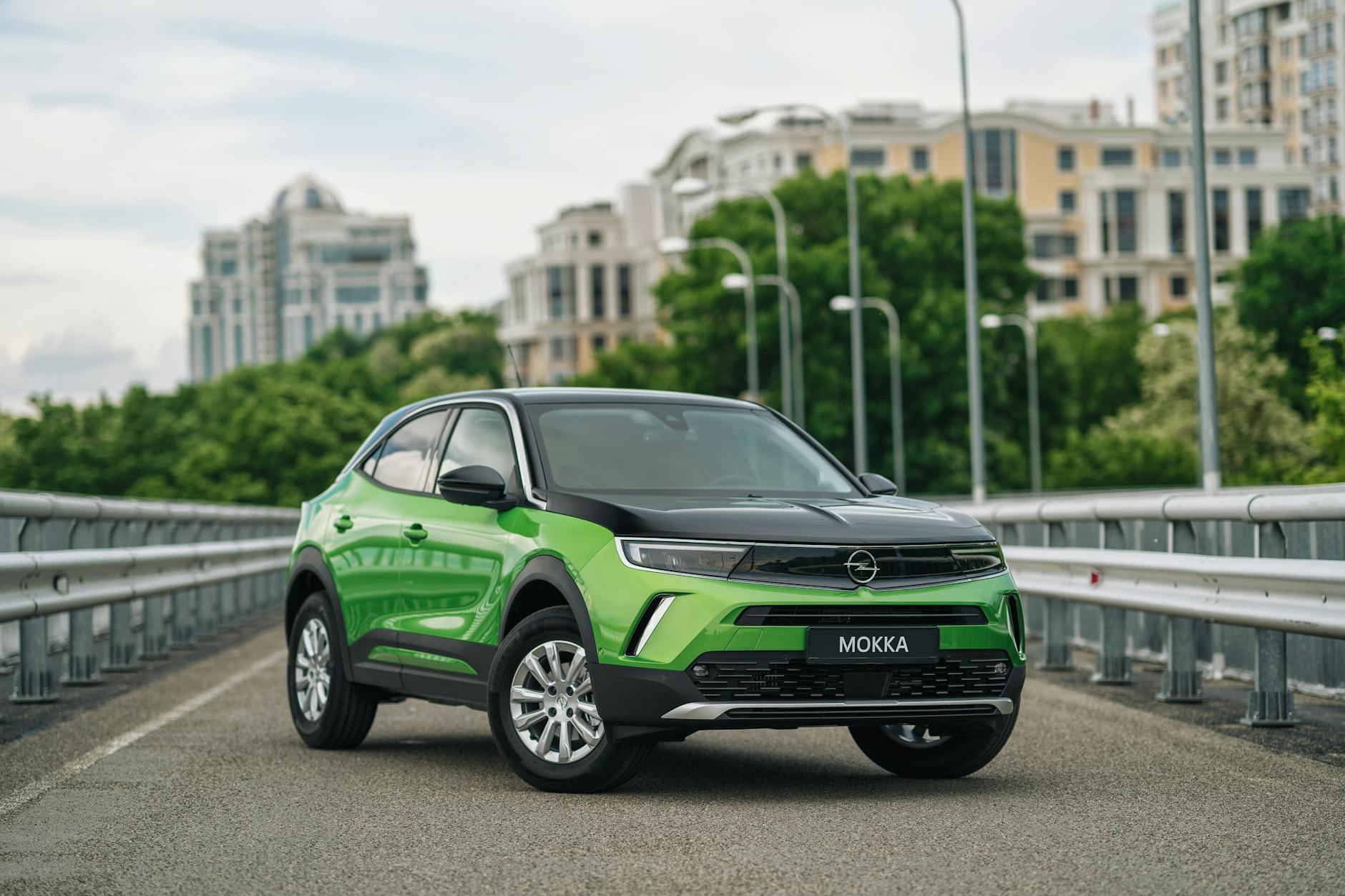 Bright green Opel Mokka-e parked on an urban bridge with cityscape backdrop.