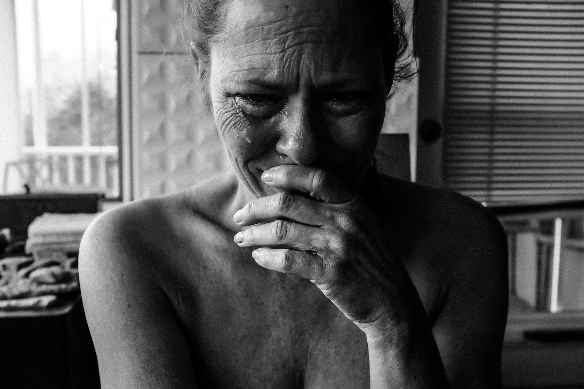 Candid black and white photo of a senior woman expressing deep emotion indoors.
