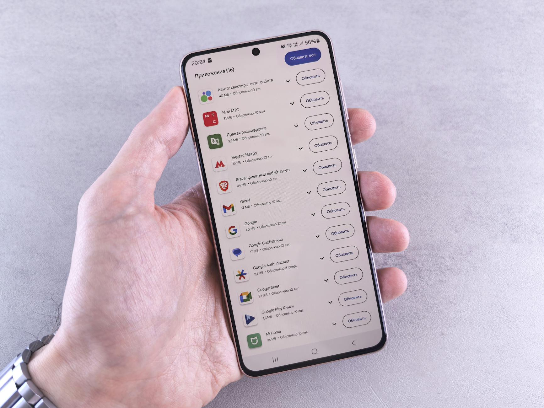 Close-up of a hand holding a smartphone displaying app updates on a light background.