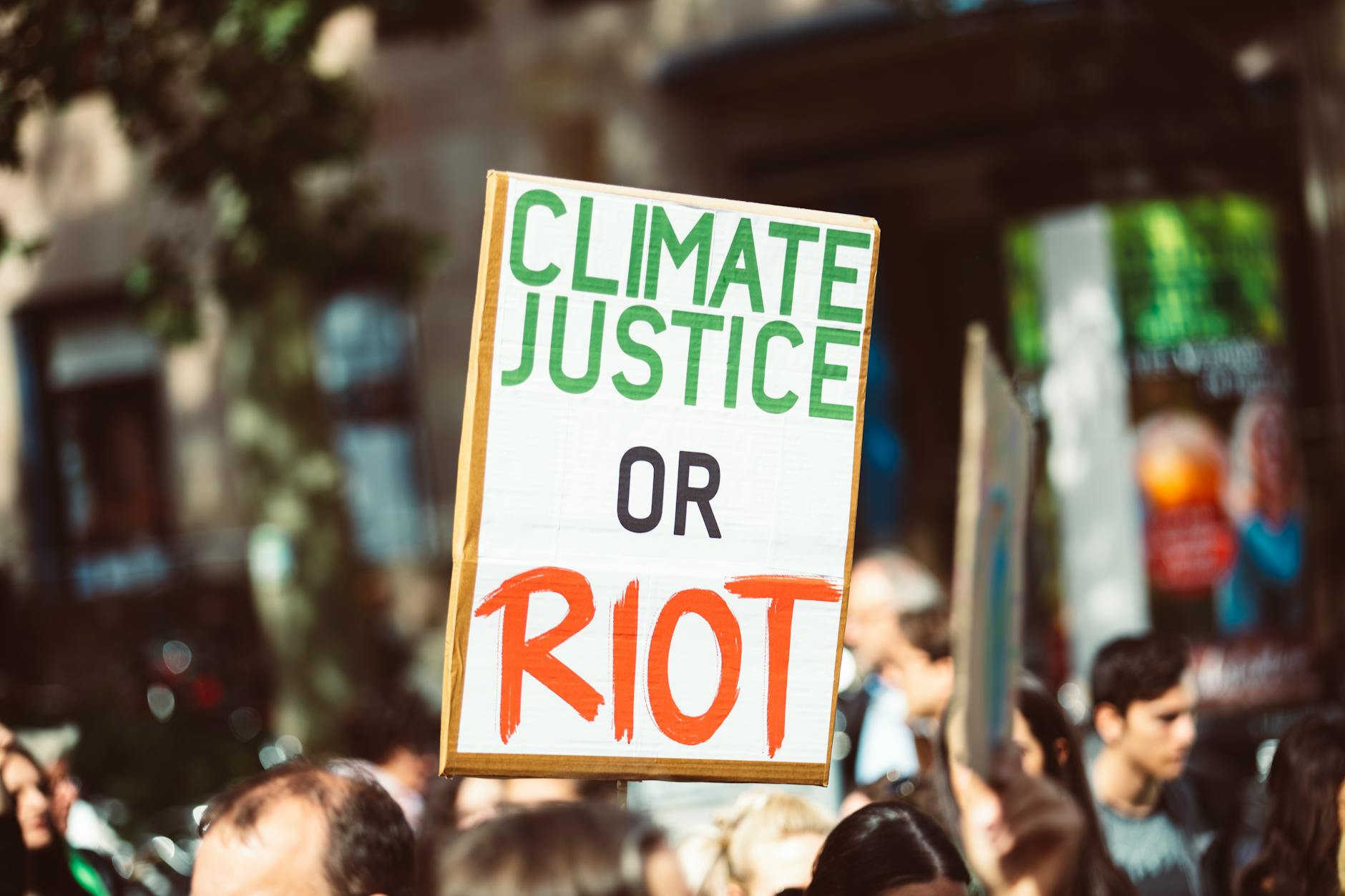 Como as alterações climáticas influenciam eventos de cheia em Portugal 4 Close-up of a protest sign reading 'Climate Justice or Riot' in a street rally focused on climate change.