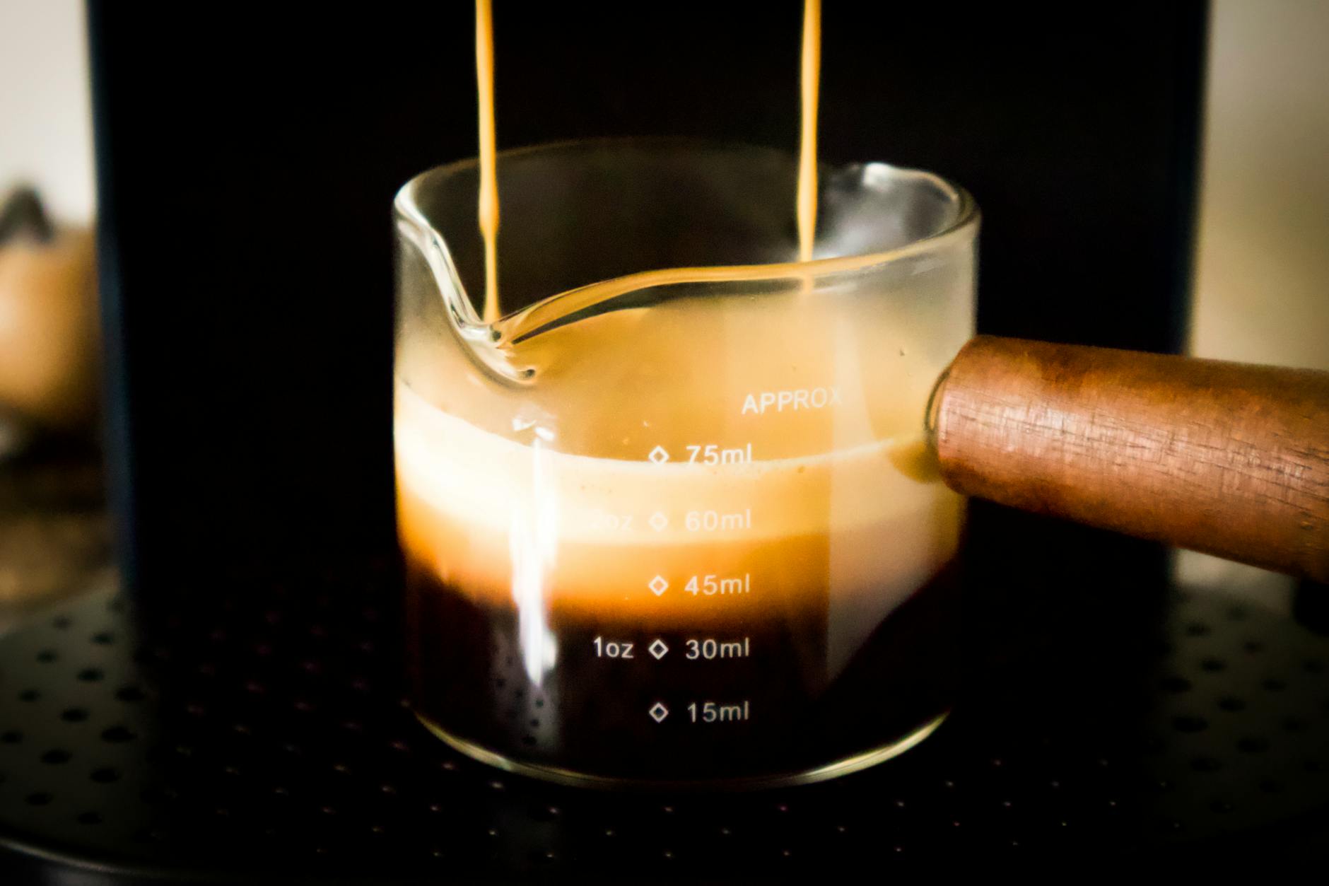 Close-up of espresso brewing into a glass cup with crema, showcasing rich coffee textures.