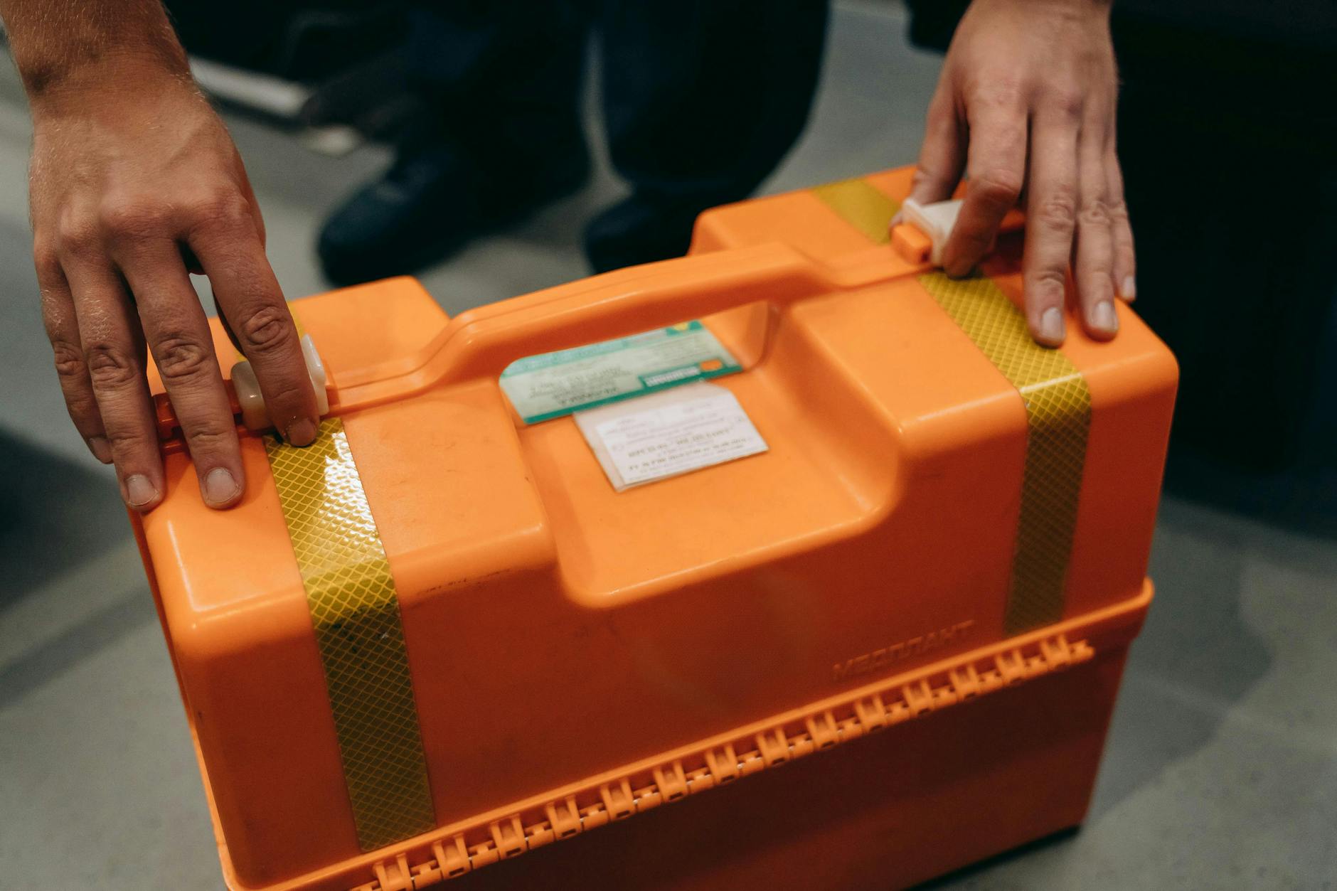 Close-up of hands holding an orange emergency medical kit indoors.
