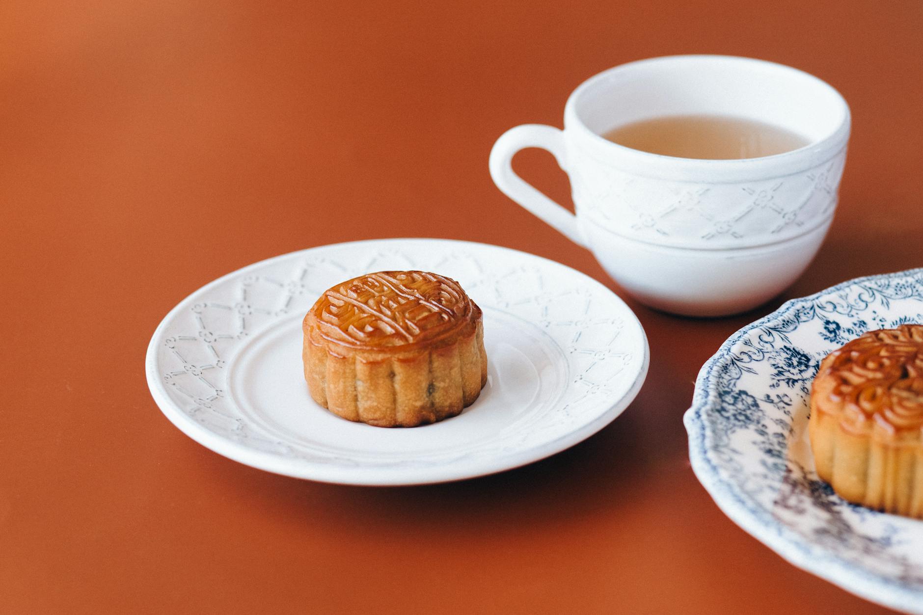 Close-up of traditional mooncakes served on white ceramic plates with a cup of tea, perfect for Mid-Autumn Festival.
