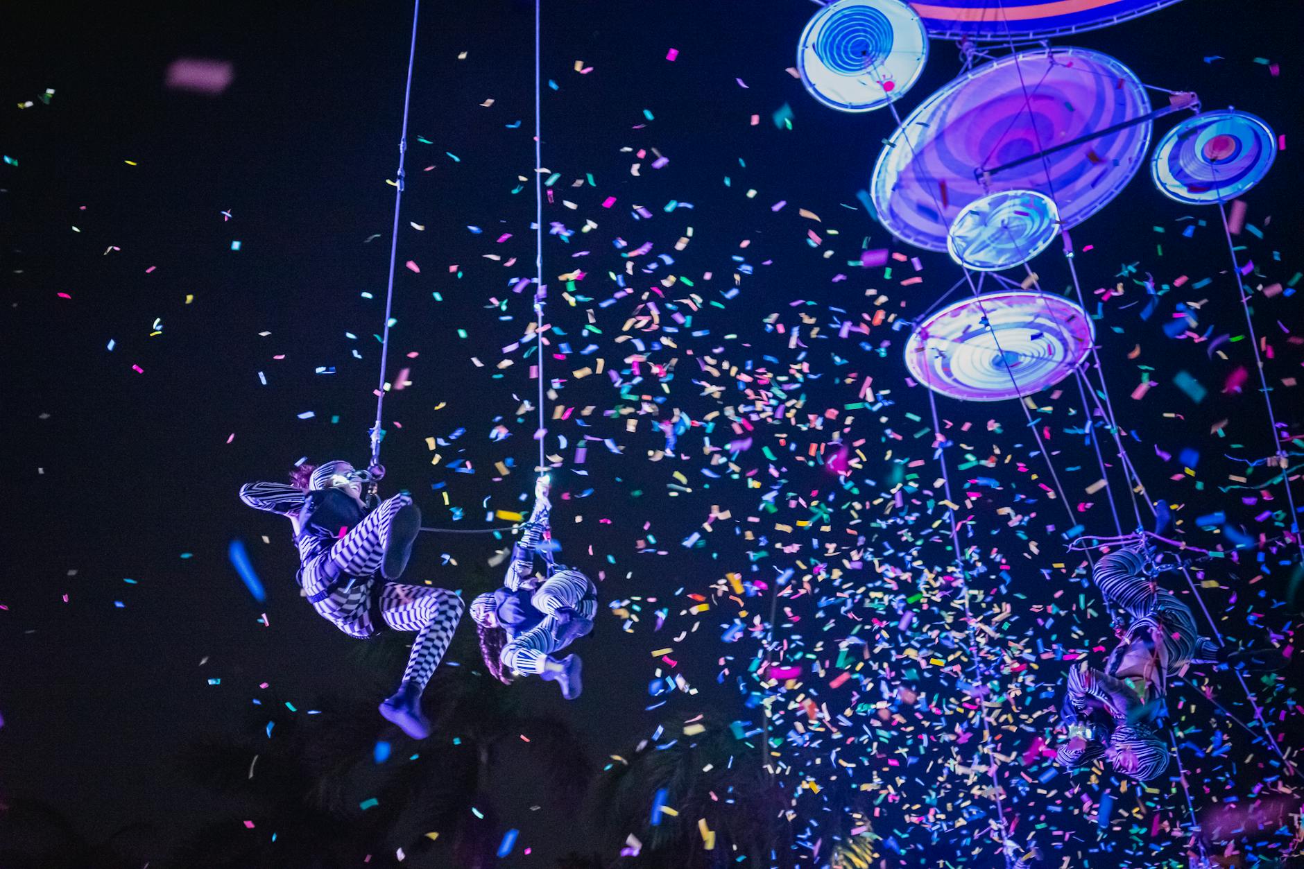 Colorful aerial acrobats performing at night with confetti shower, capturing festival magic in Merida, Mexico.